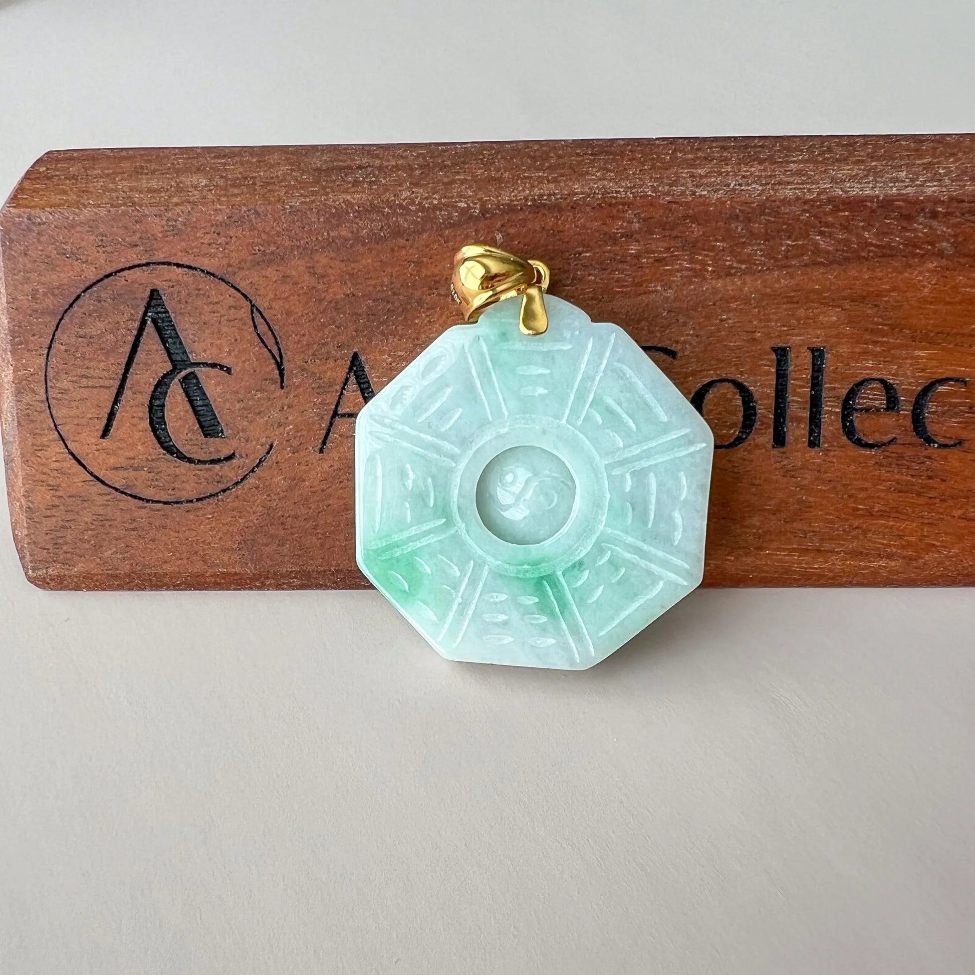 Front view of carved pale green jade pendant on wood display with gold bail