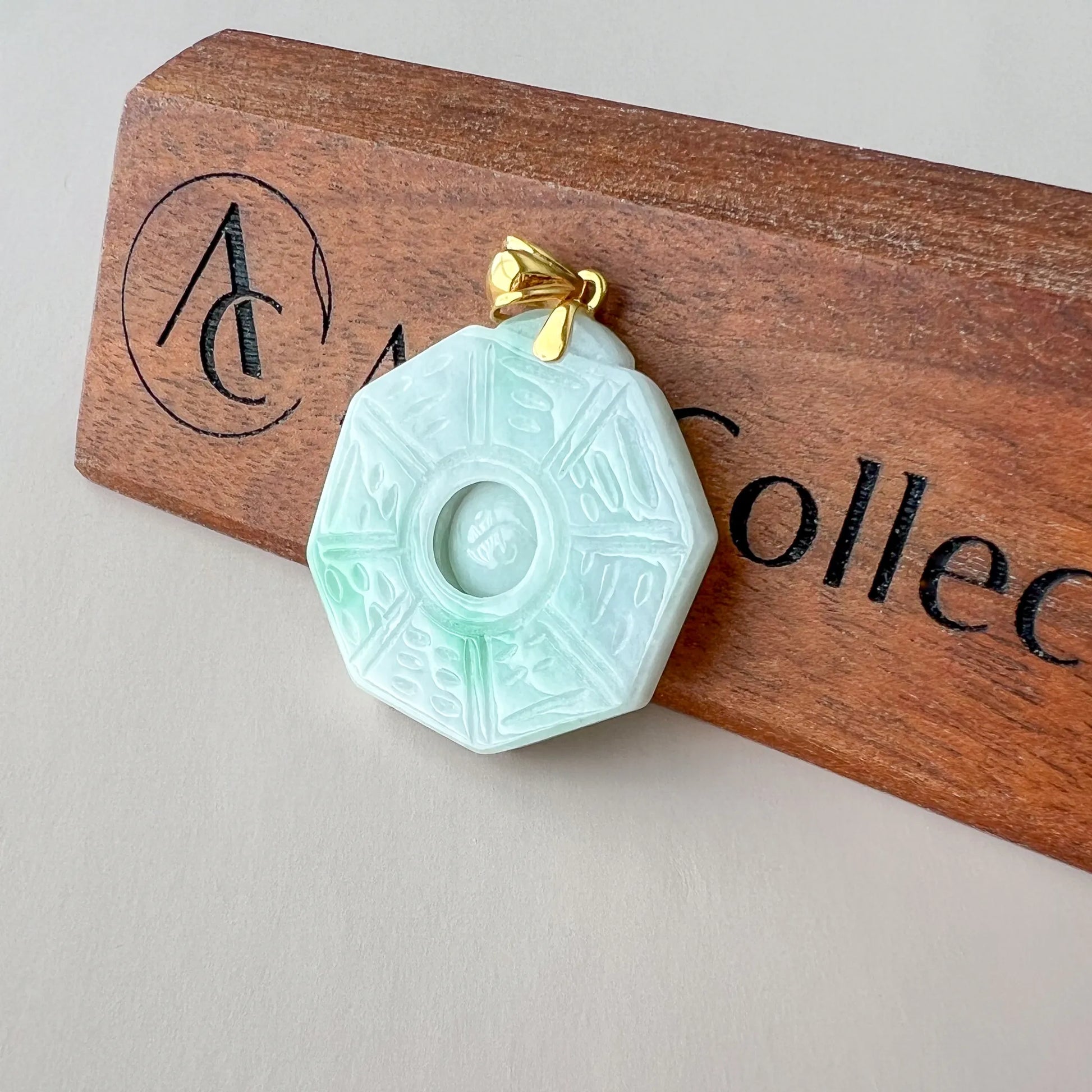 Angled front view of octagonal jade pendant with etched details and gold bail