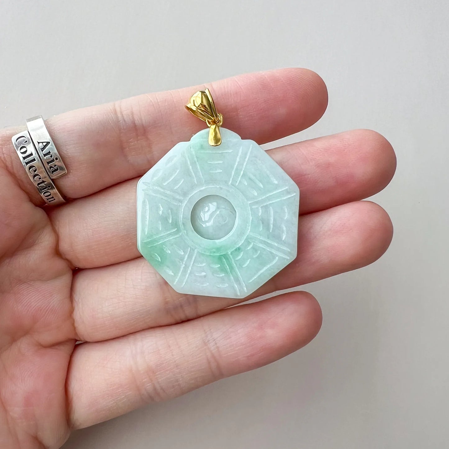 Handheld front view of light green jade pendant with polished gold bail