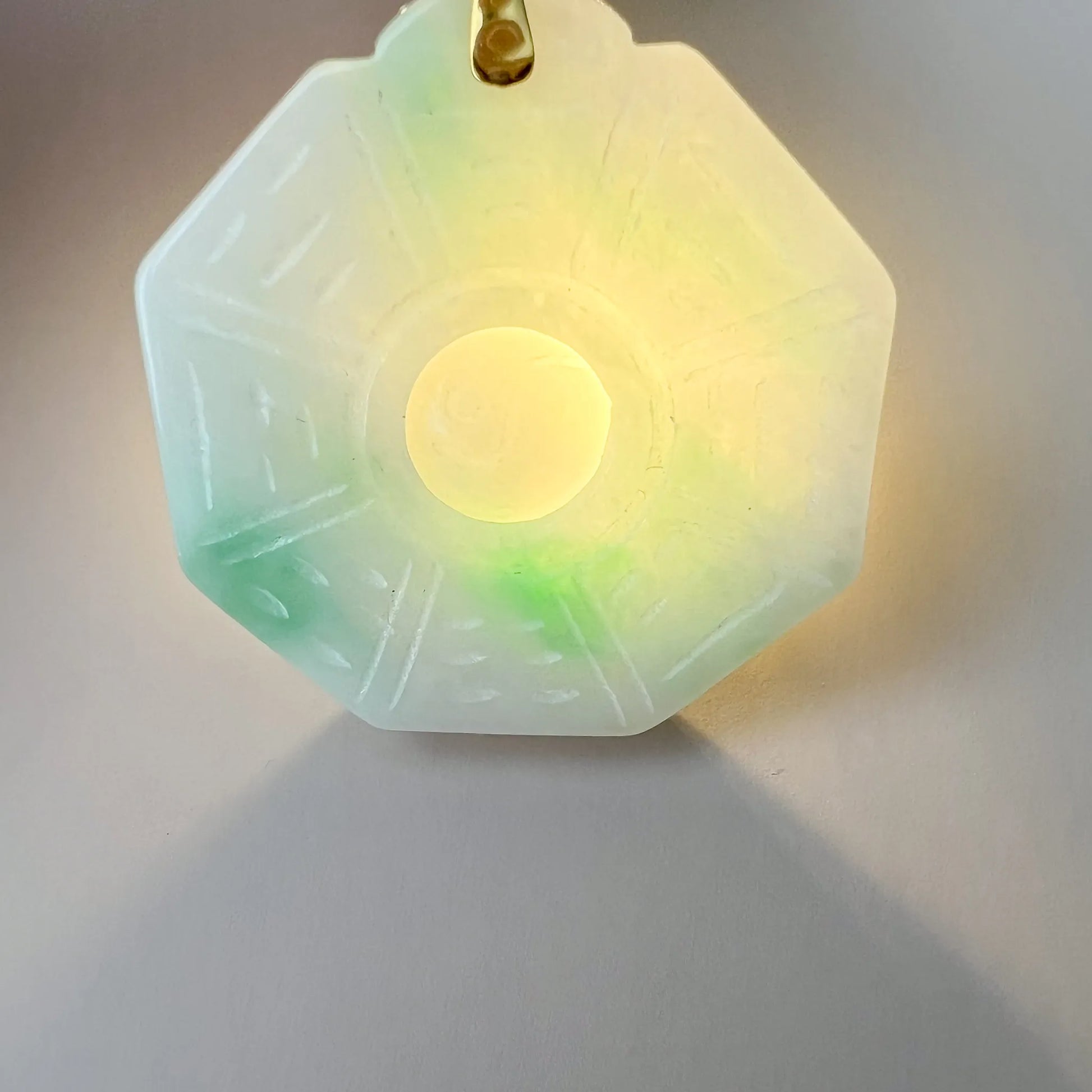 Backlit view showing translucent light green Natural Jade pendant, carved reverse, and gold-tone bail