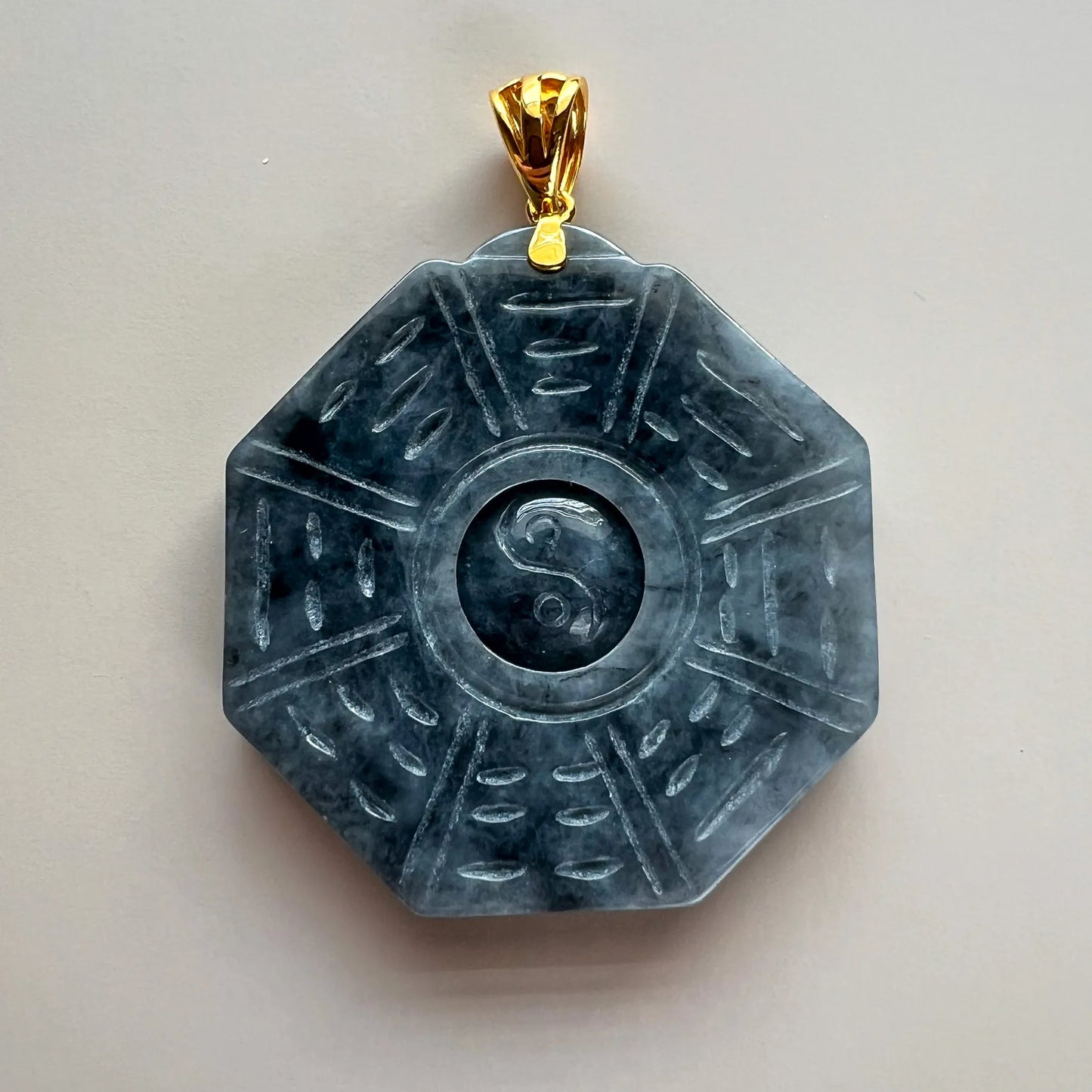 Front view of carved dark stone pendant with gold bail on neutral background