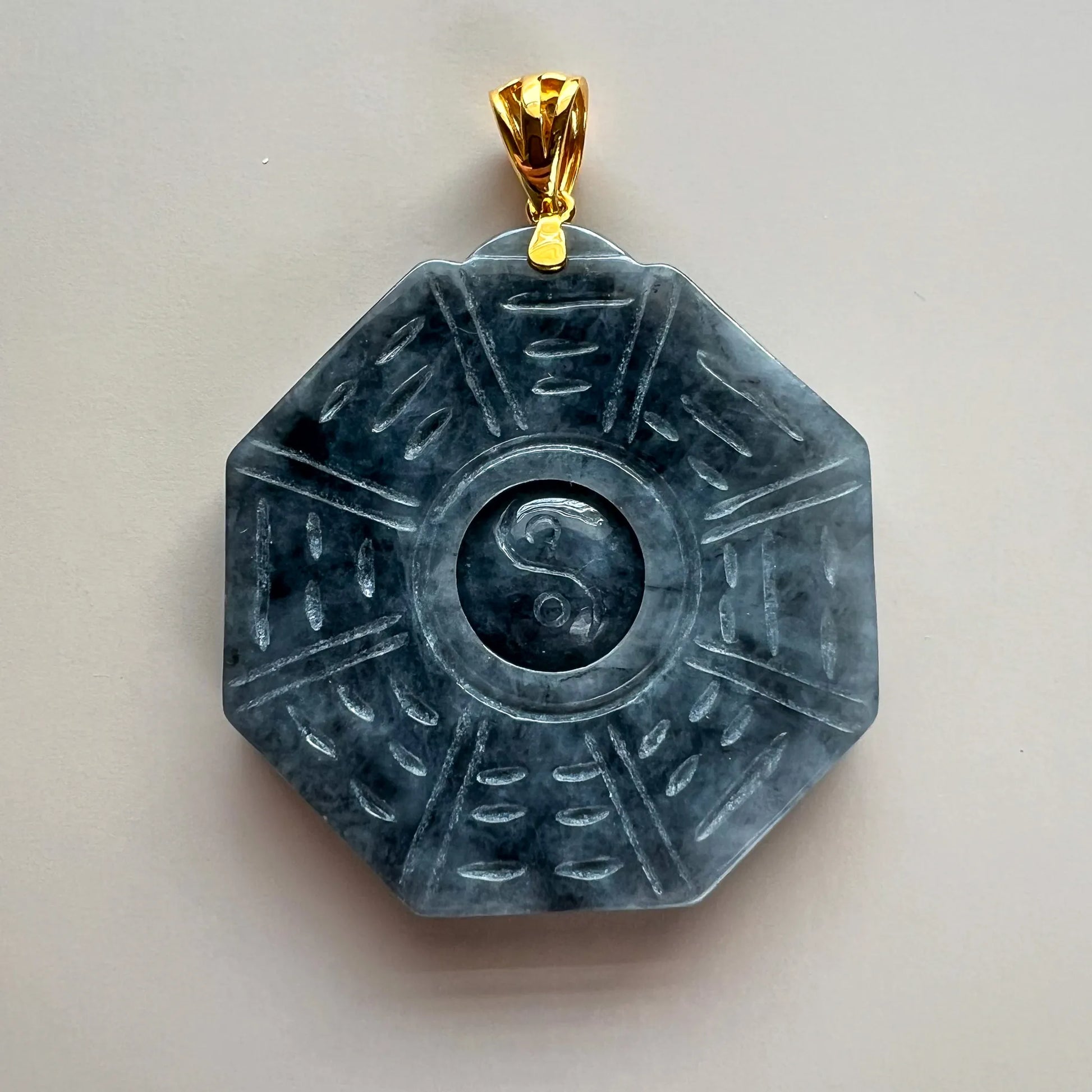 Front view of carved dark stone pendant with gold bail on neutral background
