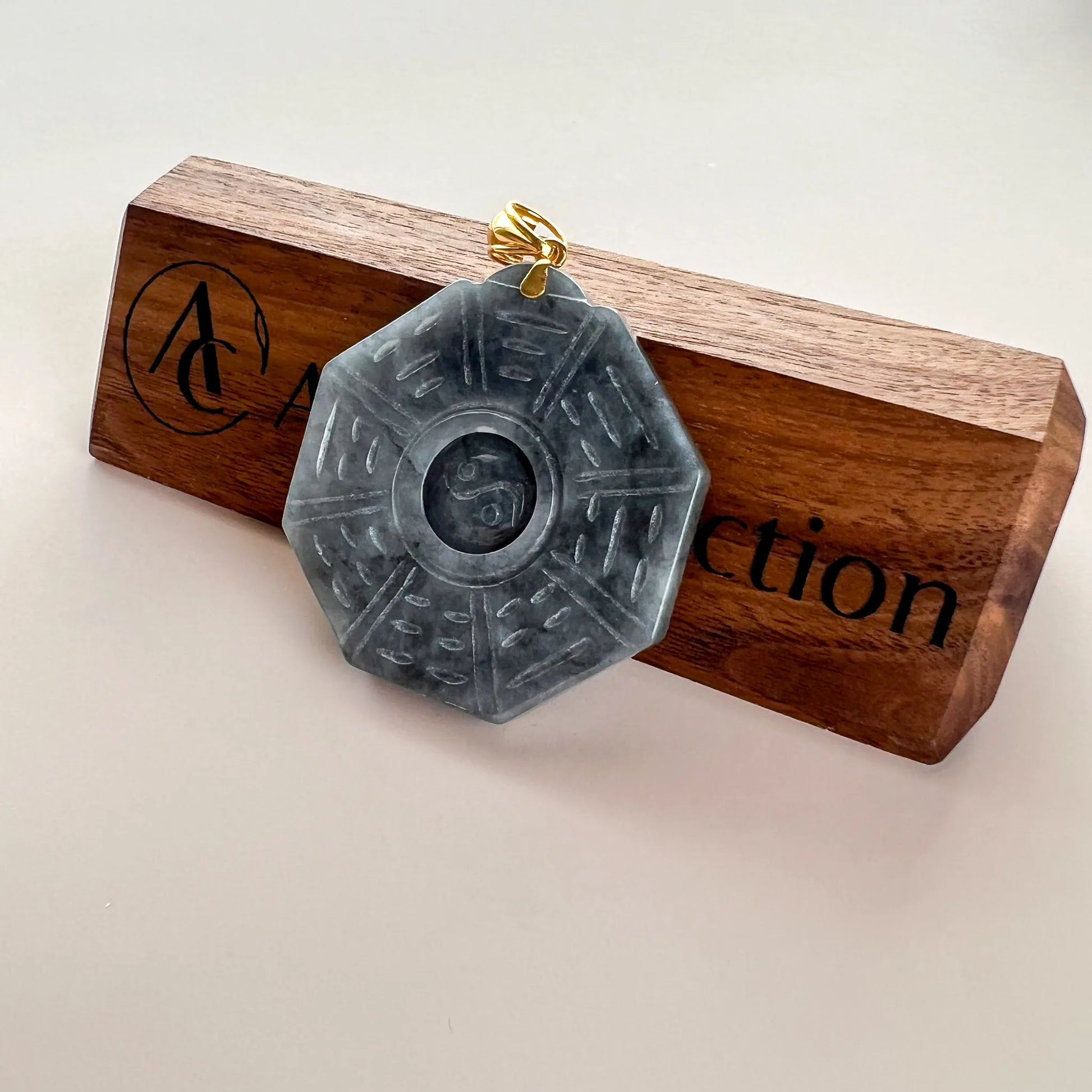 Pendant shown on wooden display stand, octagonal carved stone with polished gold bail