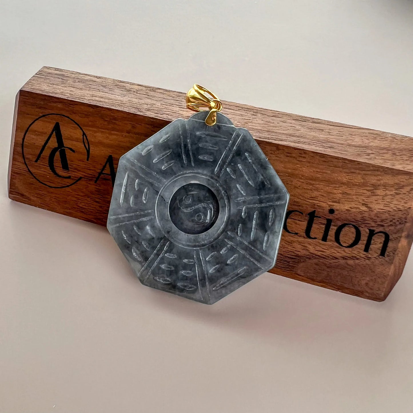 Octagonal jade pendant displayed on wooden stand, front face with yin-yang carving