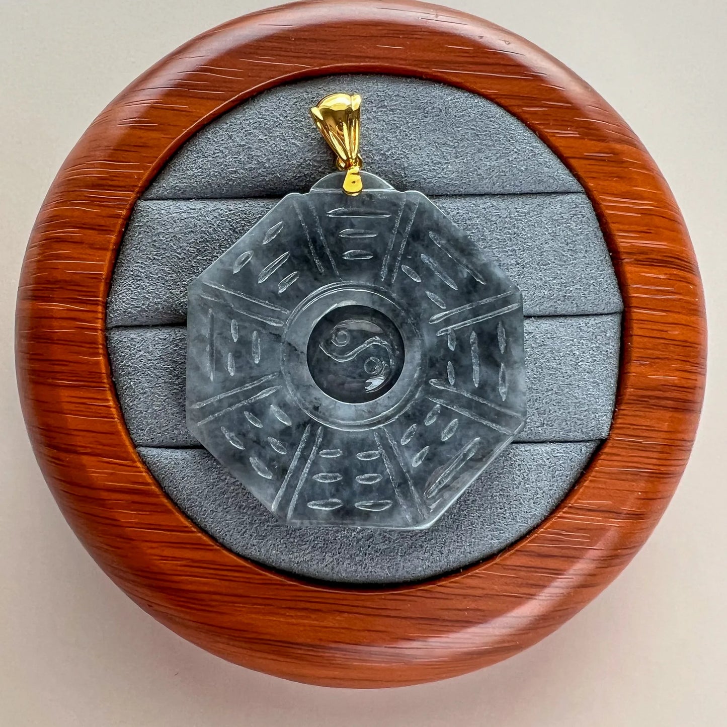 Carved stone pendant in round wooden case, front view with gold bail and protective lining