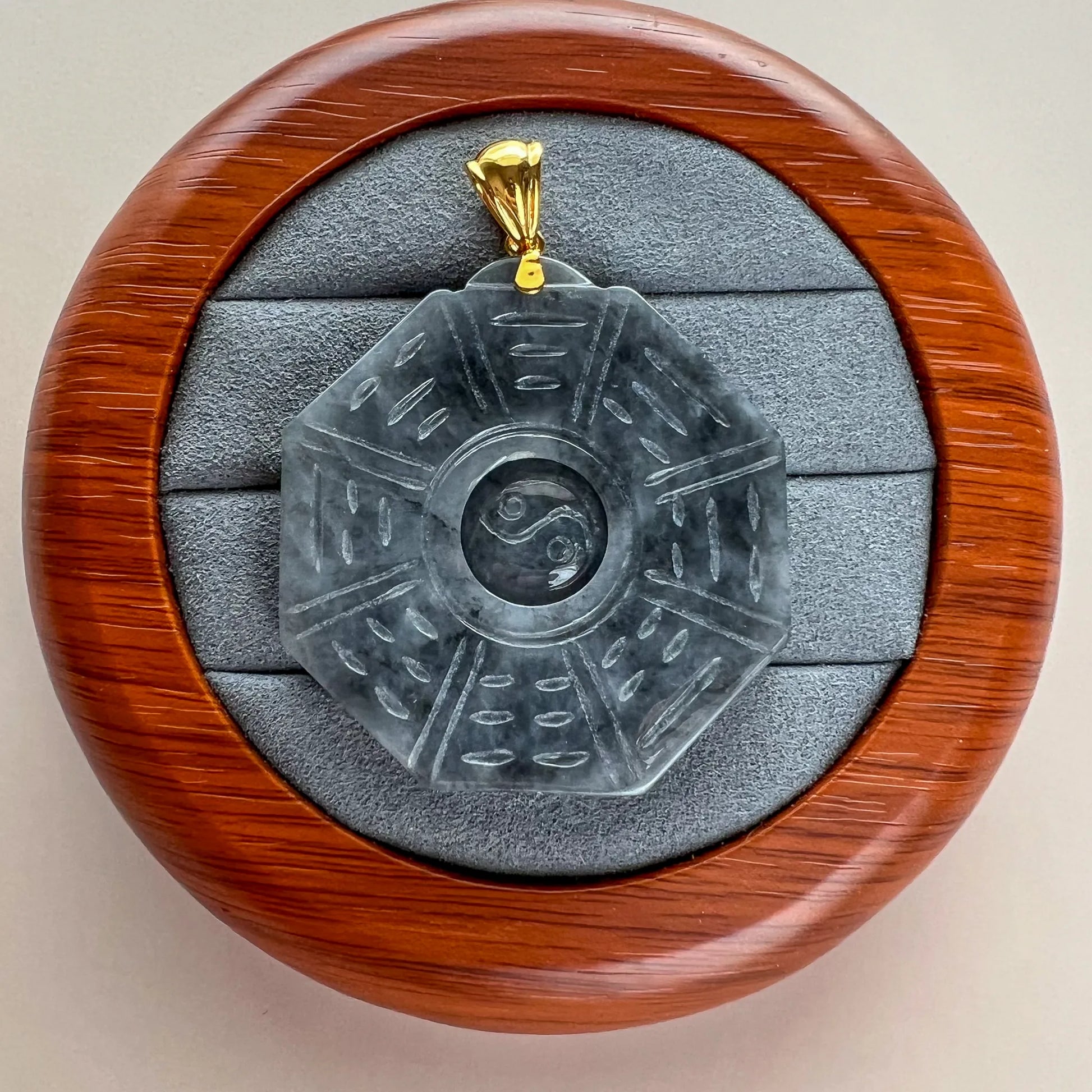 Carved stone pendant in round wooden case, front view with gold bail and protective lining