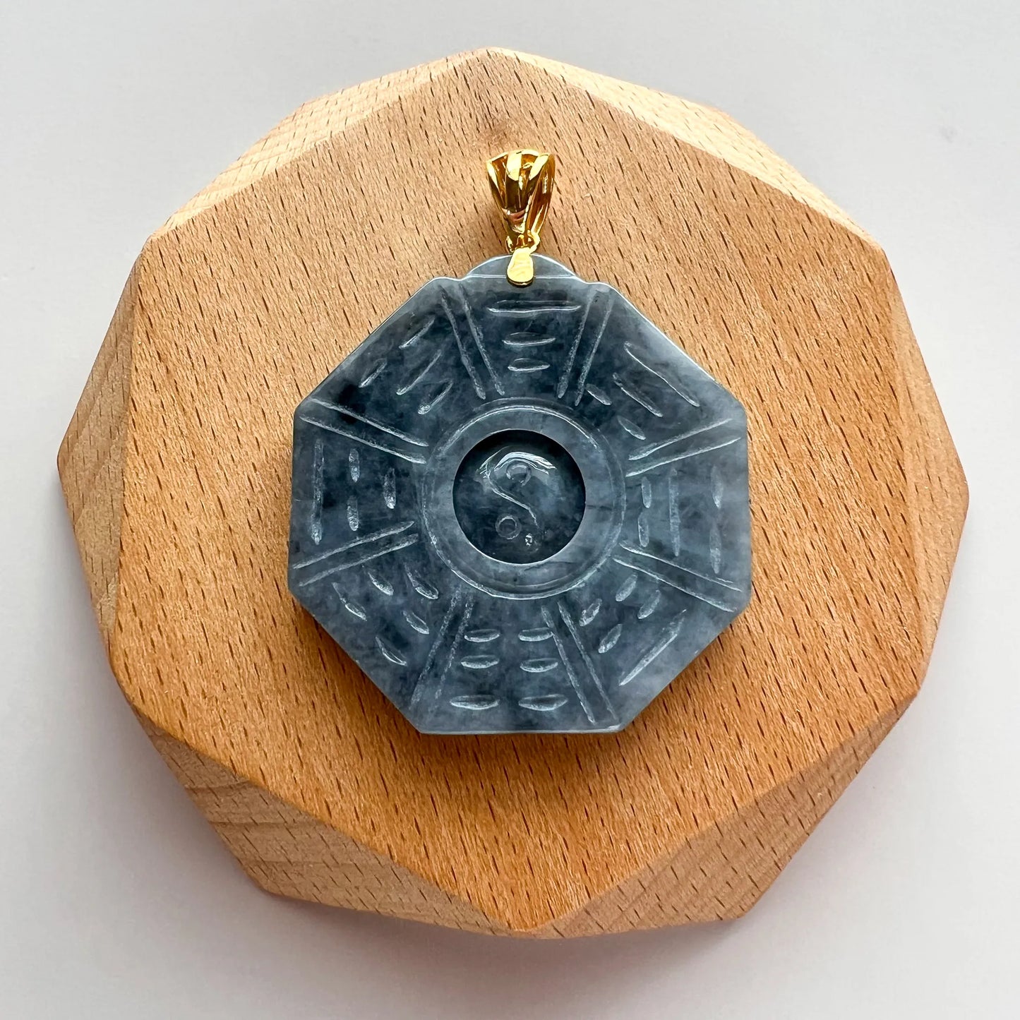 Front view of octagonal carved stone pendant on light wood display base with gold bail