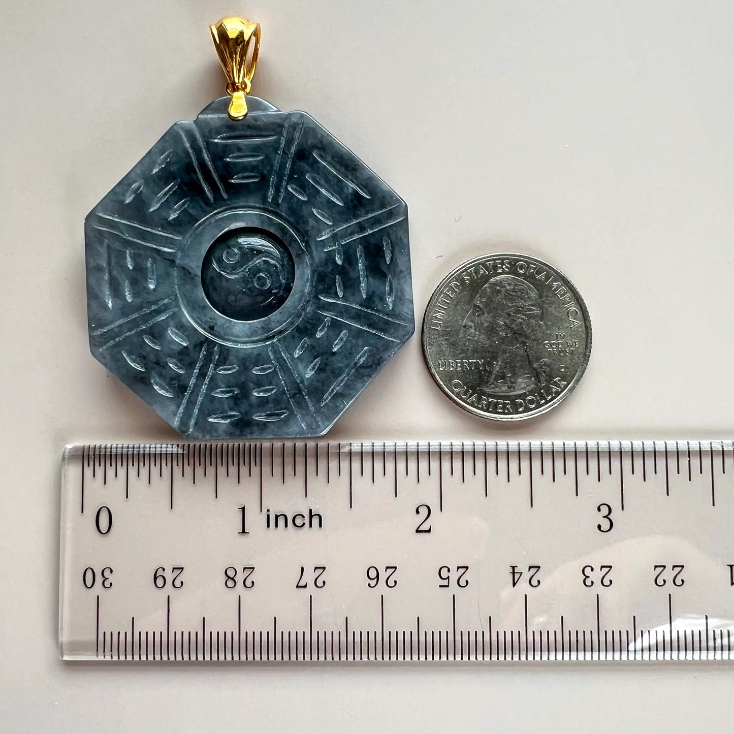 Front view of octagonal natural jade pendant beside a ruler and quarter for scale