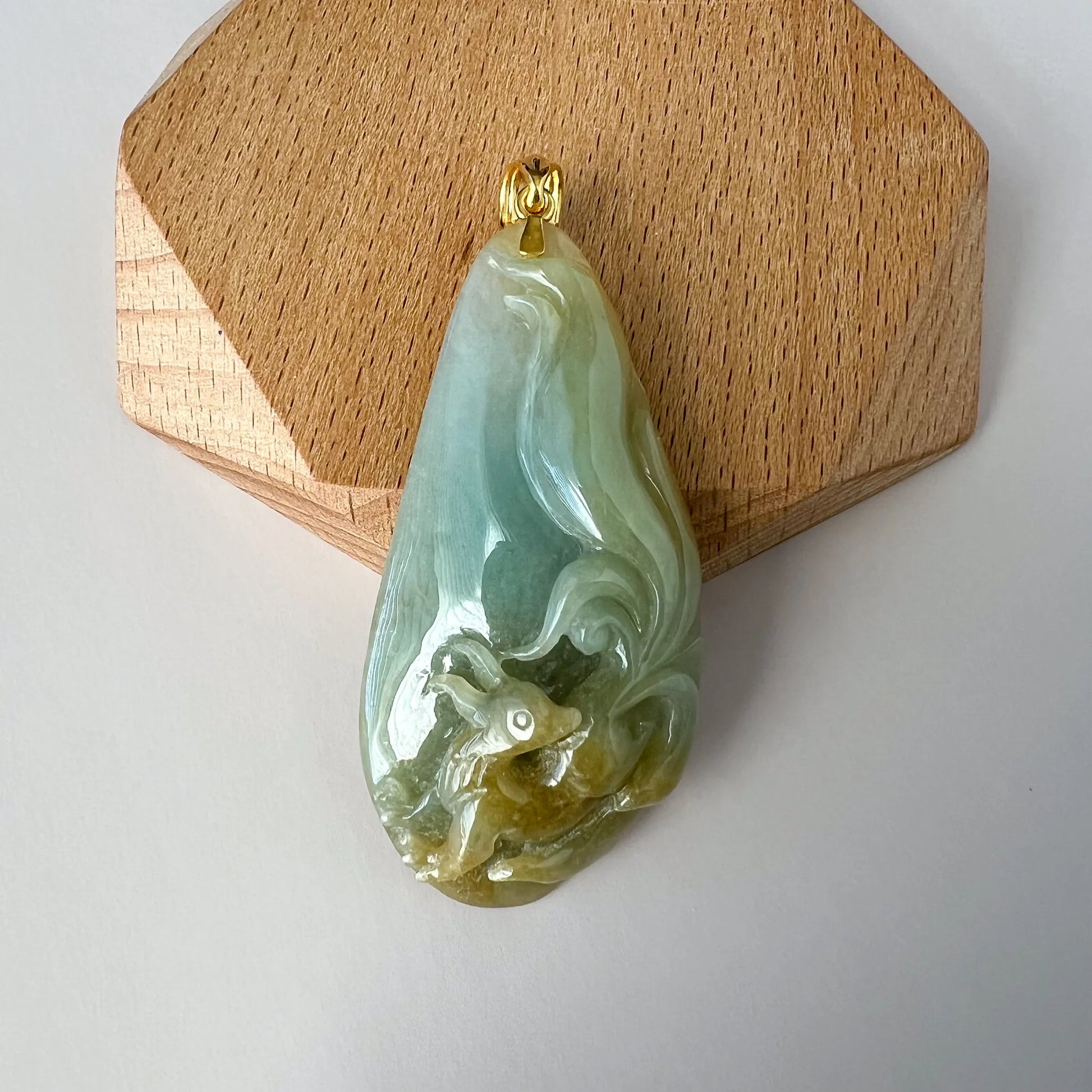 Front view of carved green jade pendant with gold bail on display stand