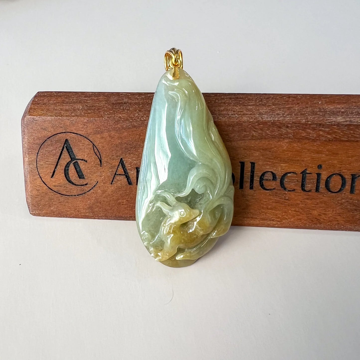 Front view of polished jade pendant with gold bail against branded wooden block