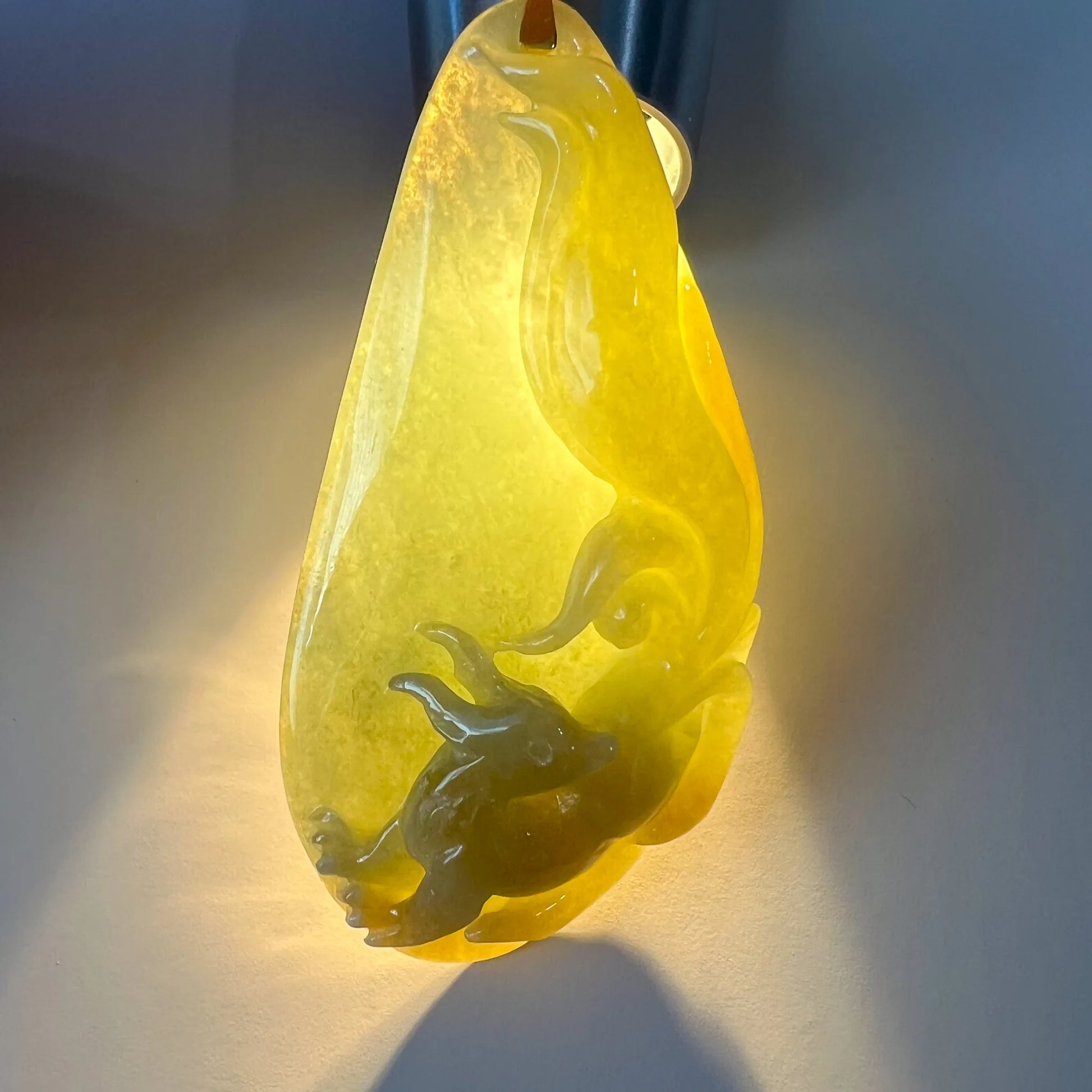 Backlit view of translucent yellow-green jade pendant highlighting carved details