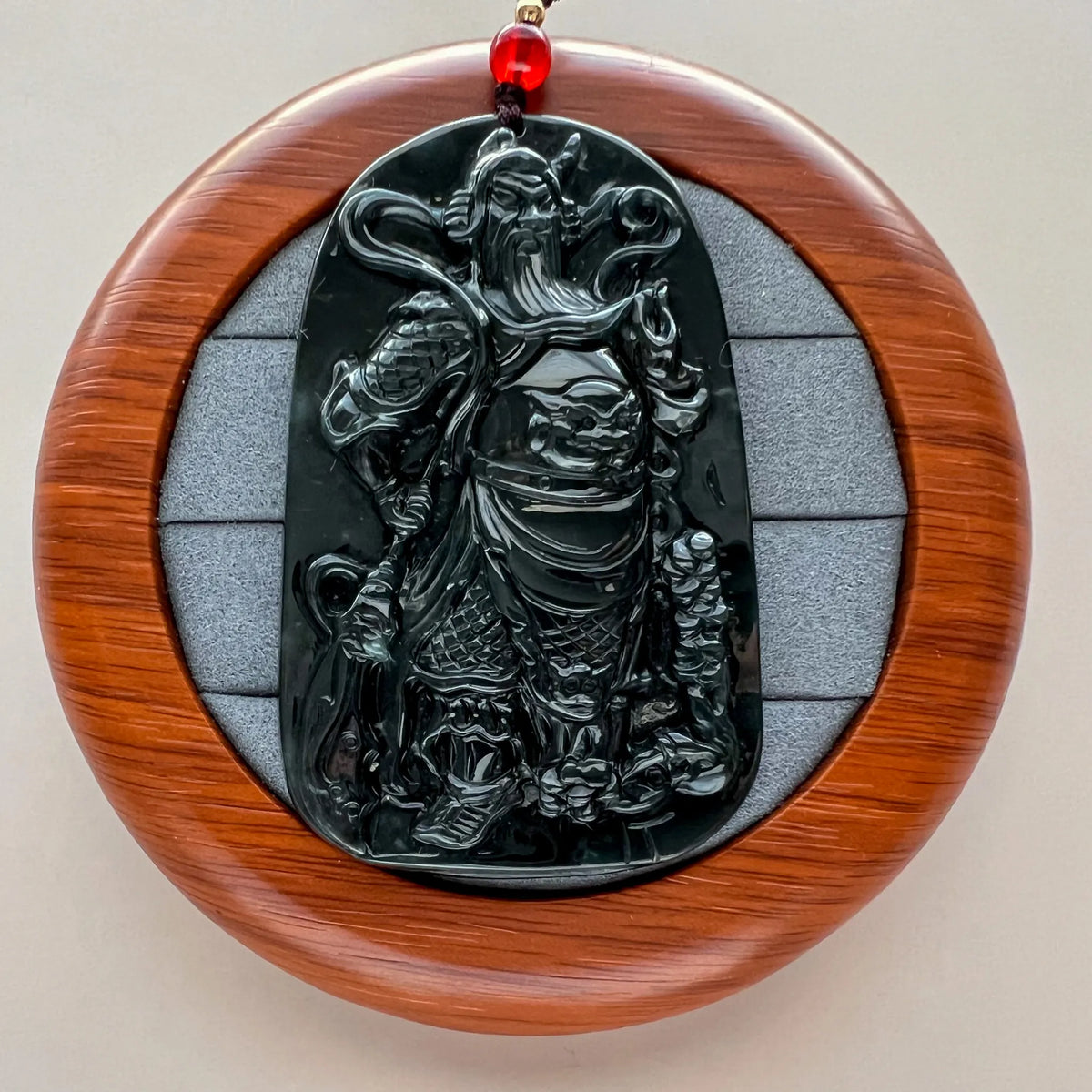 Front view of glossy black carved pendant on round wood display stand
