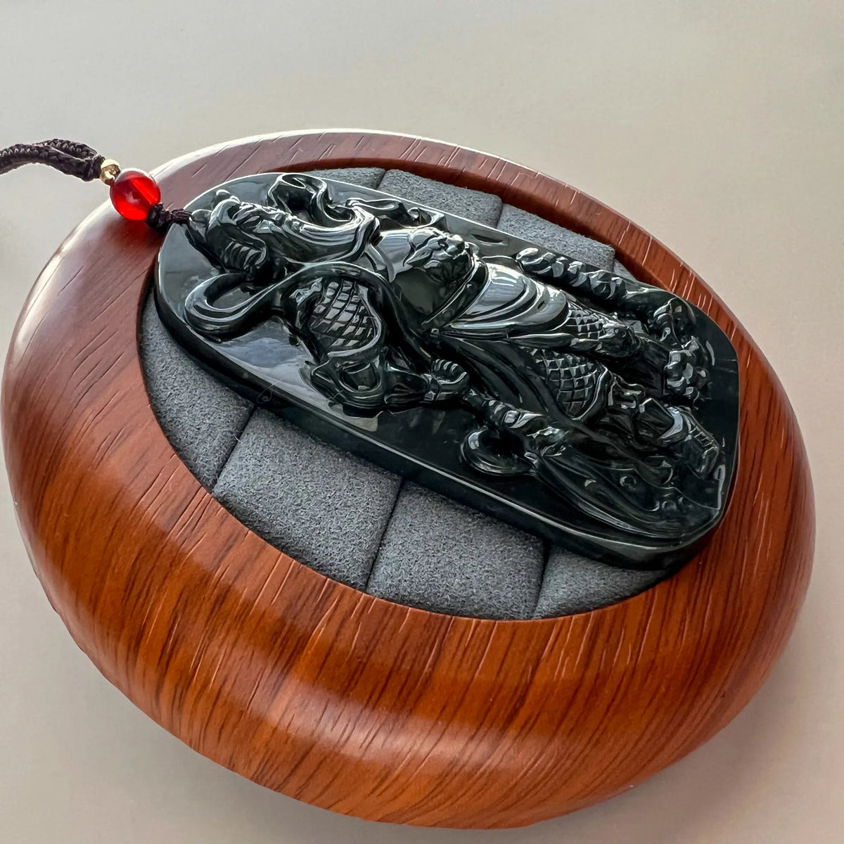 Angled side view of polished black jade pendant on wood display stand