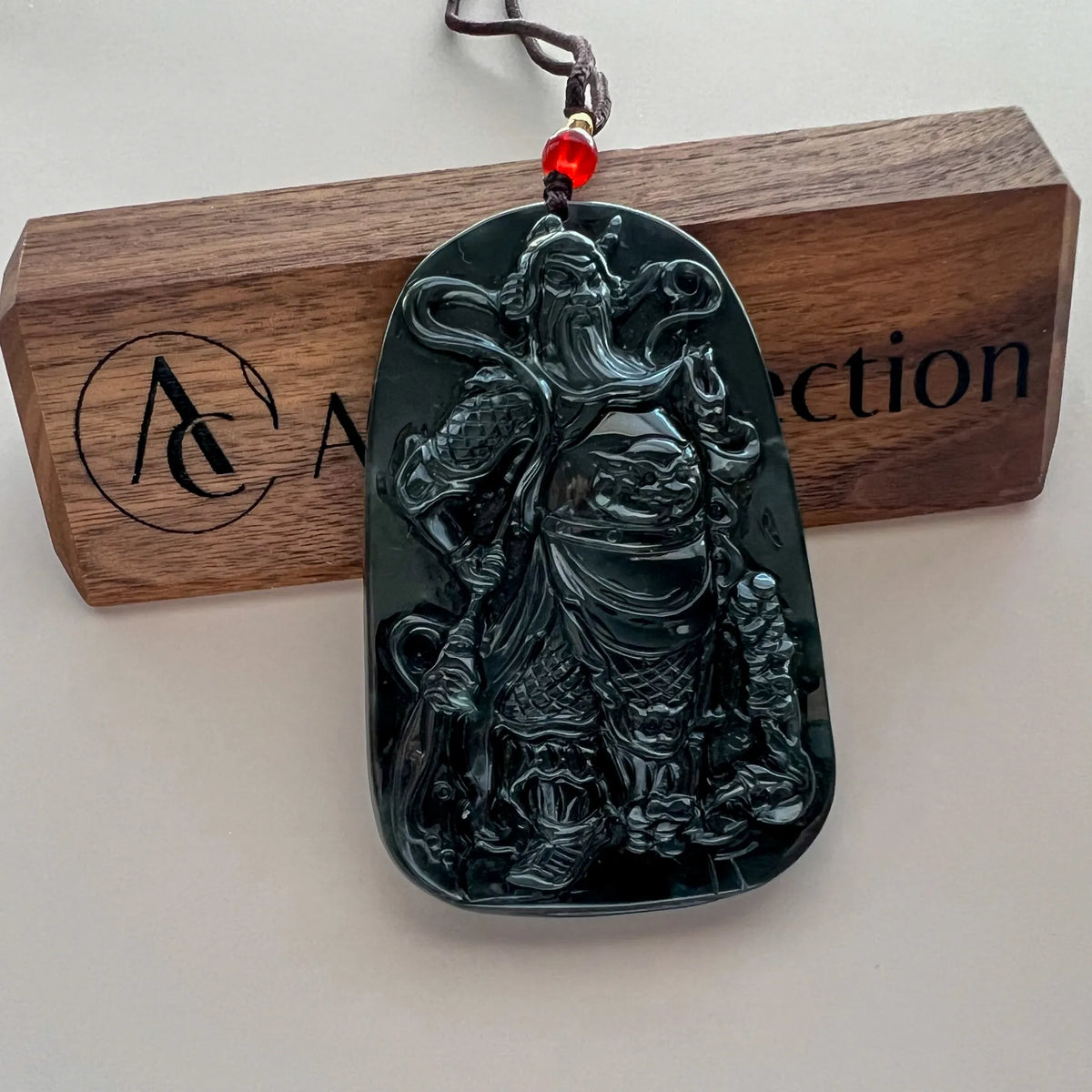 Front view of carved black jade pendant hanging against branded wood block