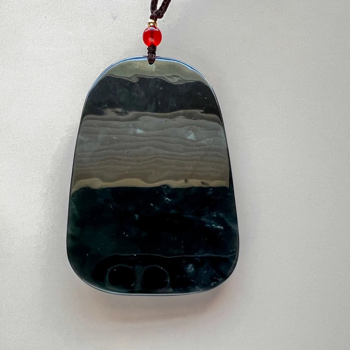 Polished reverse of dark green natural jade pendant with broad gray-green horizontal bands