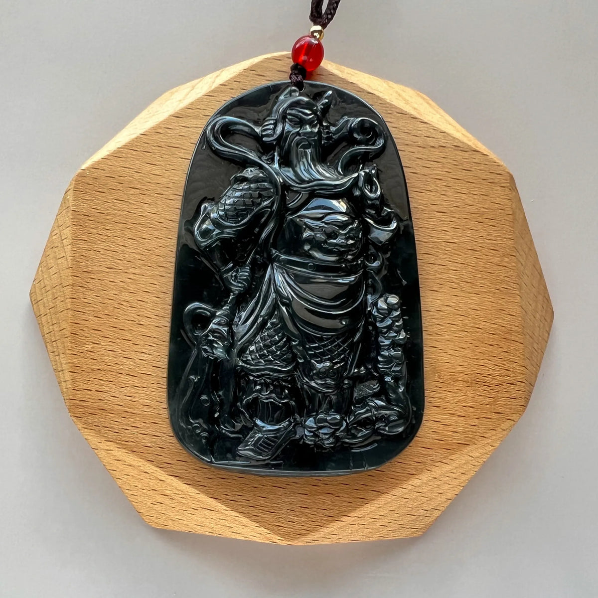 Front view of carved black pendant displayed on faceted wood stand
