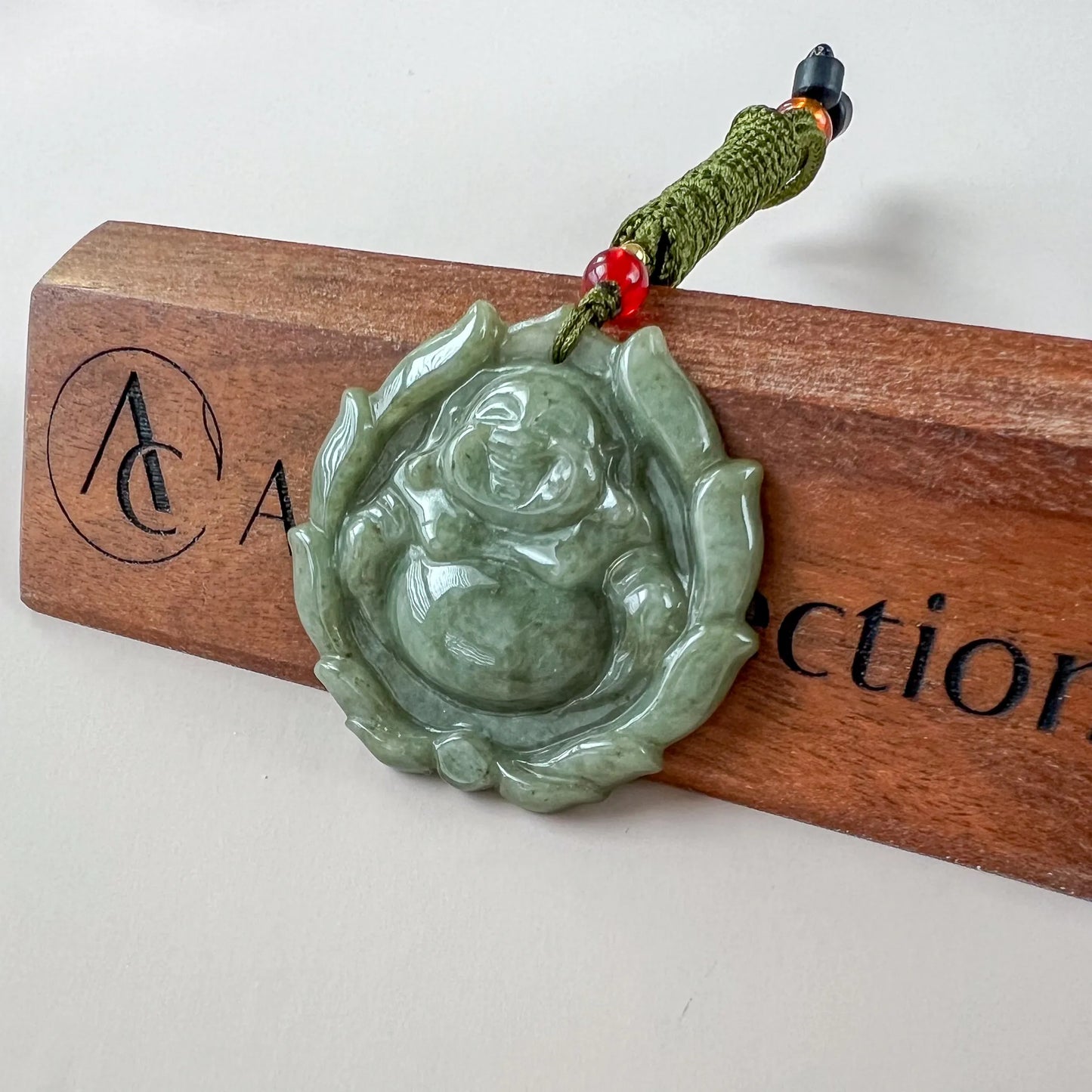 Green jadeite Happy Buddha with lotus pendant, glossy carved finish, angled on wooden display with cord detail
