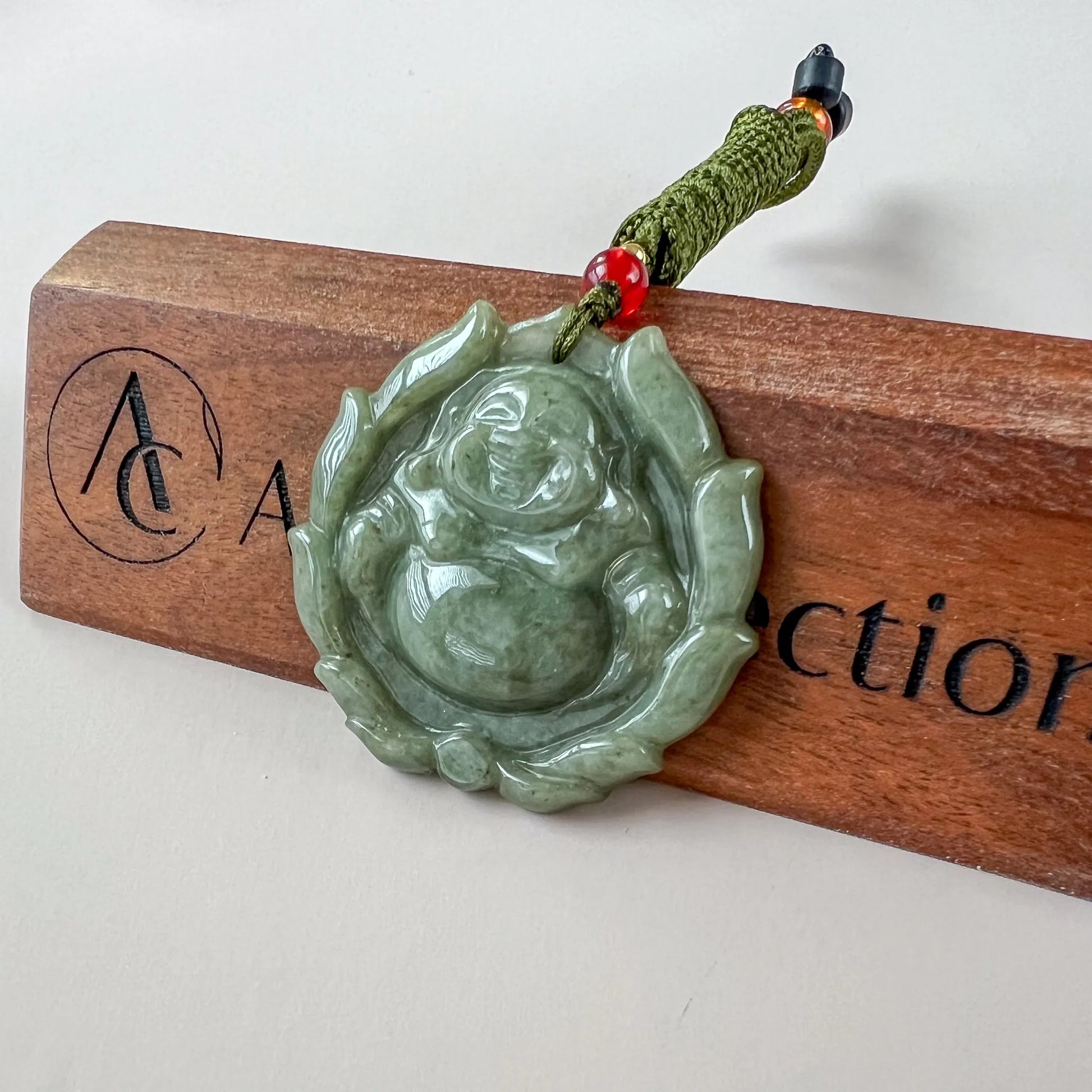 Green jadeite Happy Buddha with lotus pendant, glossy carved finish, angled on wooden display with cord detail