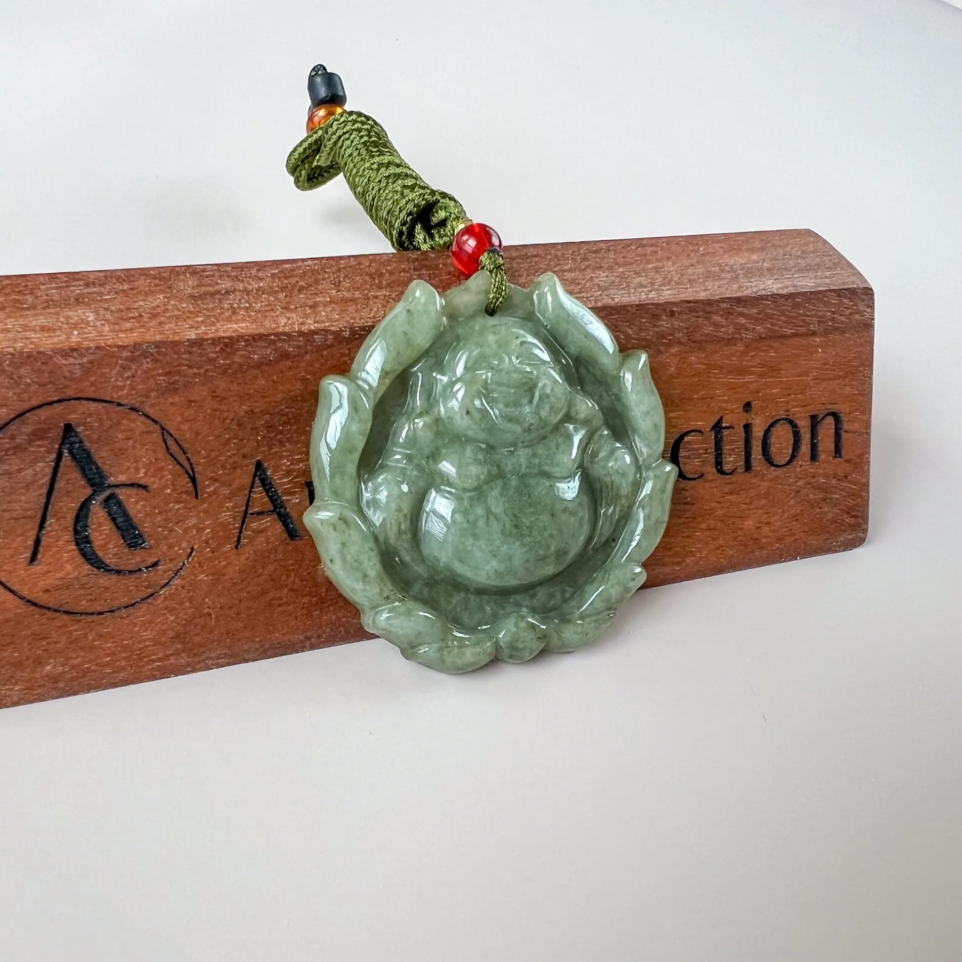 Green jadeite Happy Buddha lotus pendant with glossy carved finish, shown on a cord over a wooden display stand