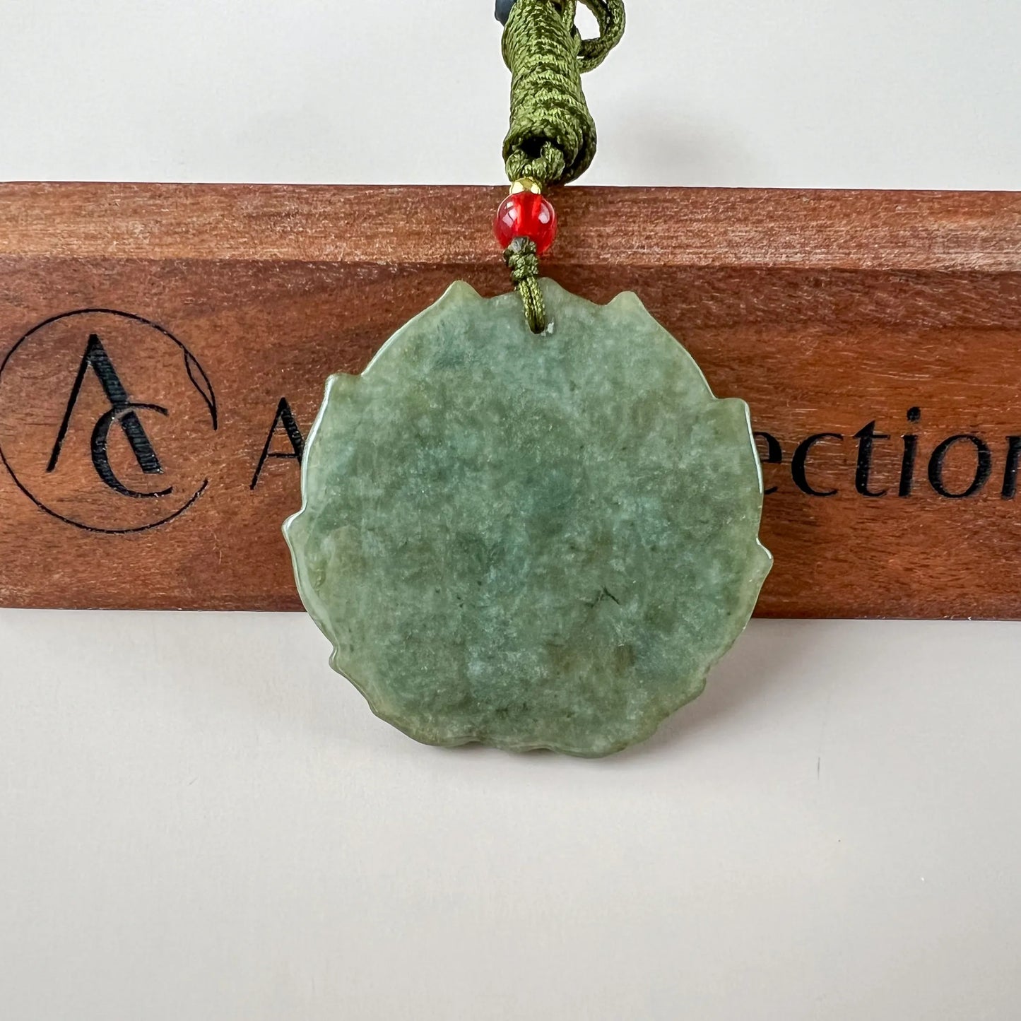 Close-up of green jadeite jade pendant with scalloped edge, polished finish, and cord bead detail on wood stand