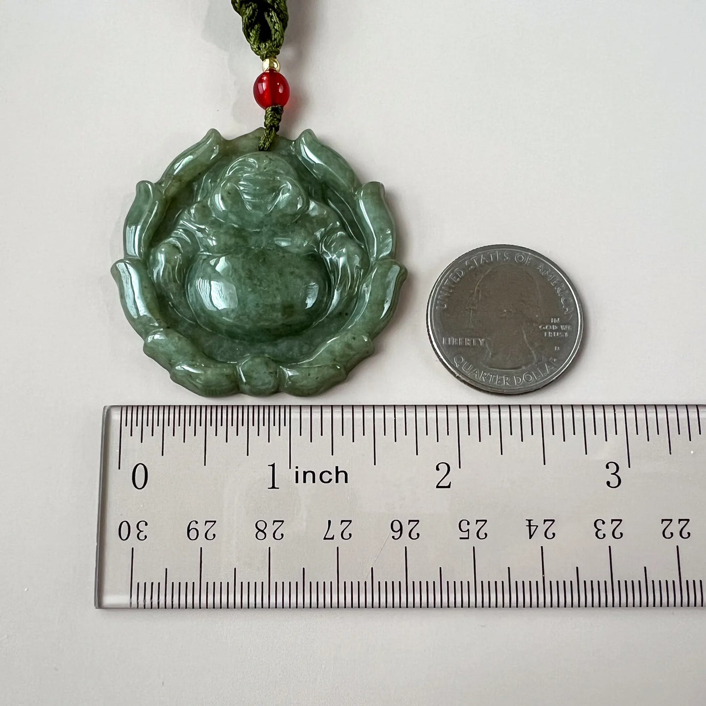 Green jadeite jade Happy Buddha with lotus pendant, polished carved front view beside ruler and quarter for scale
