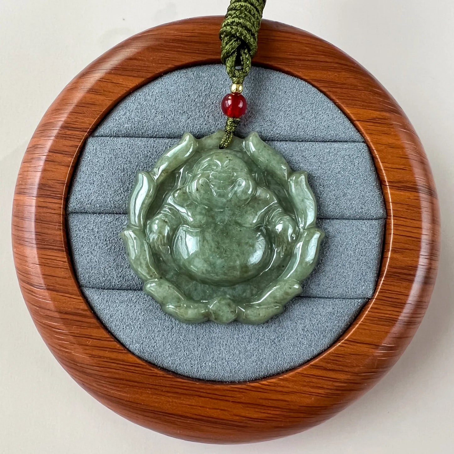 Green jadeite Happy Buddha with lotus pendant in polished wood display case, front view, glossy carved finish