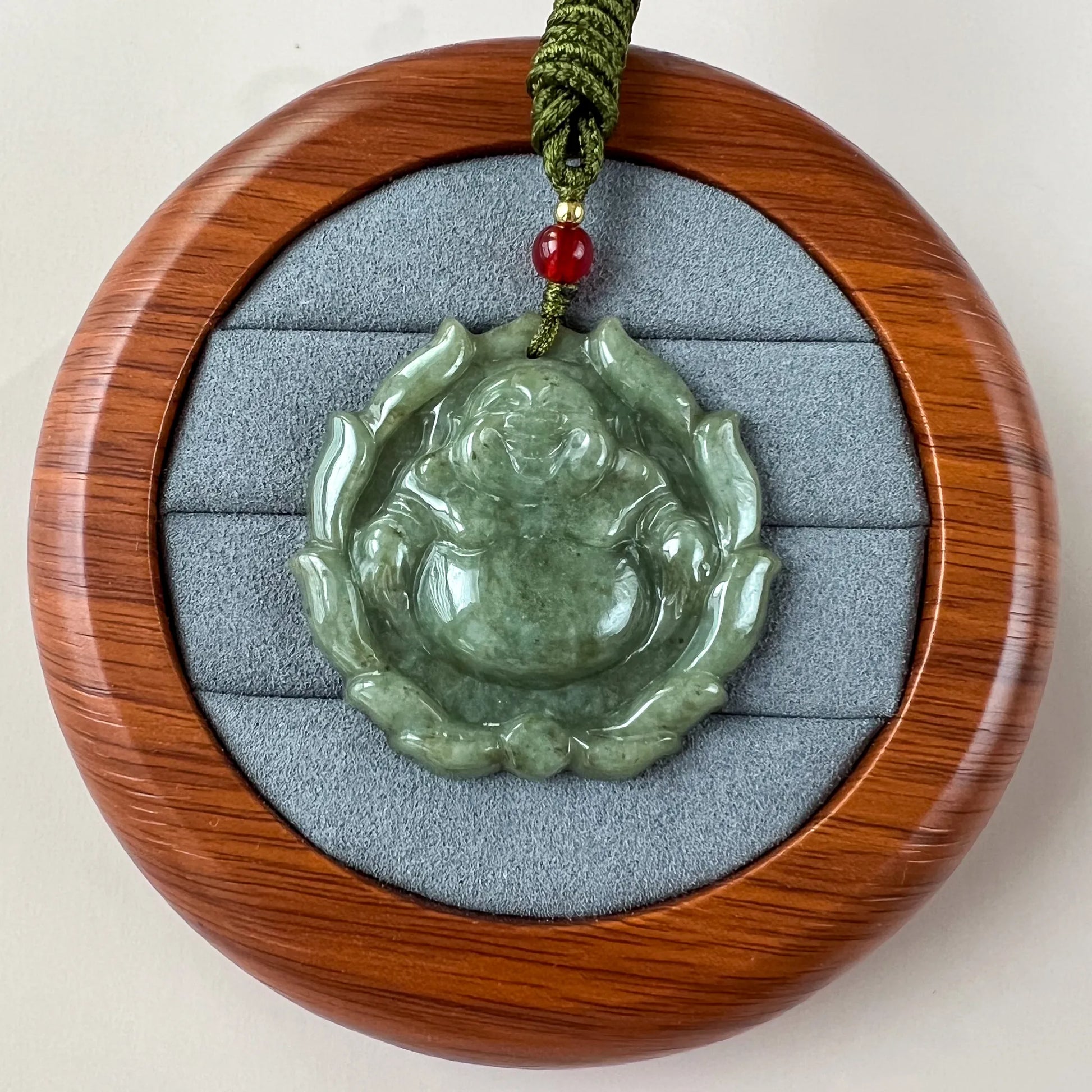 Green jadeite Happy Buddha with lotus pendant in polished wood display case, front view, glossy carved finish