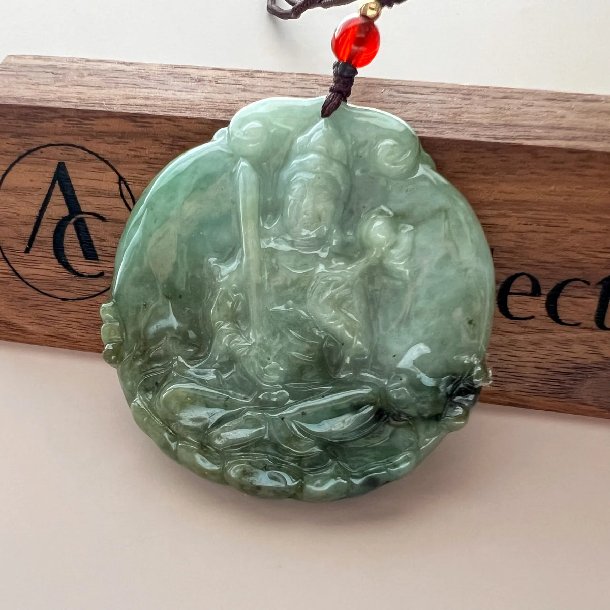 Front view of carved green jade pendant hanging on wooden display plaque, polished finish