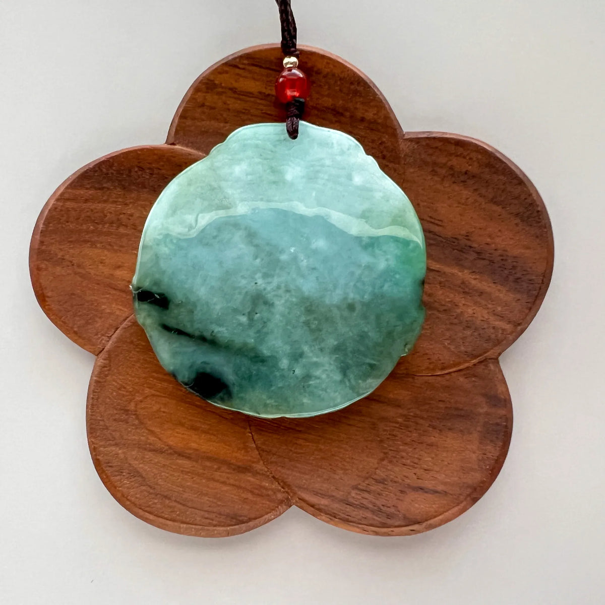 Smooth polished back of mottled light and dark green natural jade pendant with cord and red bead