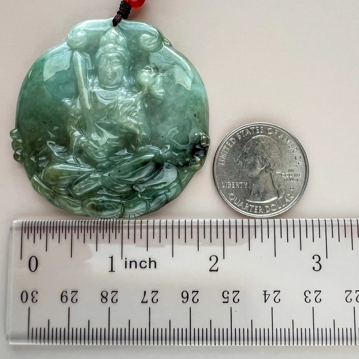 Front view with quarter for scale, glossy carved jade pendant on cord