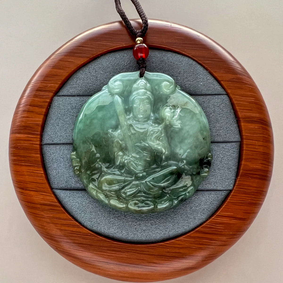Front view of carved jade pendant in round display case with wood frame and gray insert