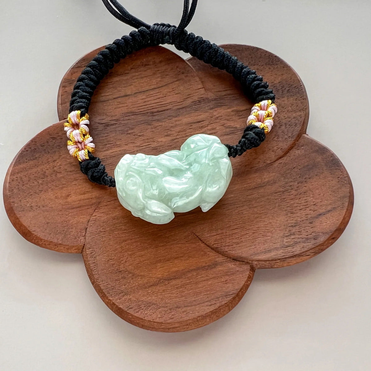 Front view of pale green carved jade charm on black woven cord bracelet