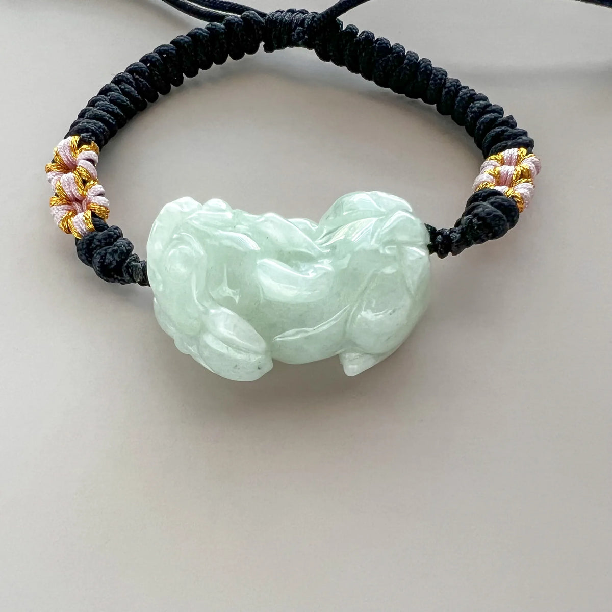 Close-up front view of polished jade charm on adjustable black cord bracelet
