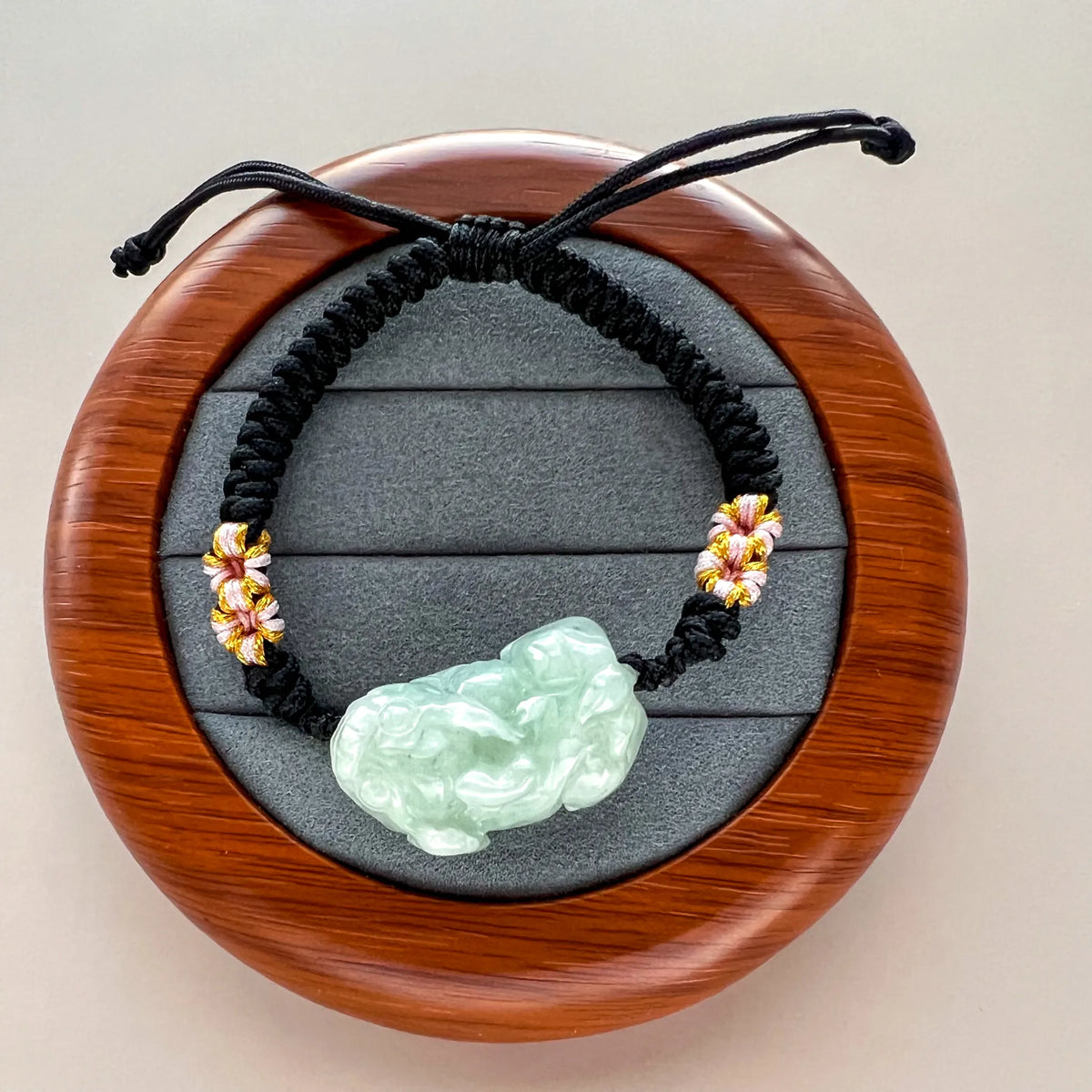 Polished light green jade carving with woven accents and adjustable black cord closure