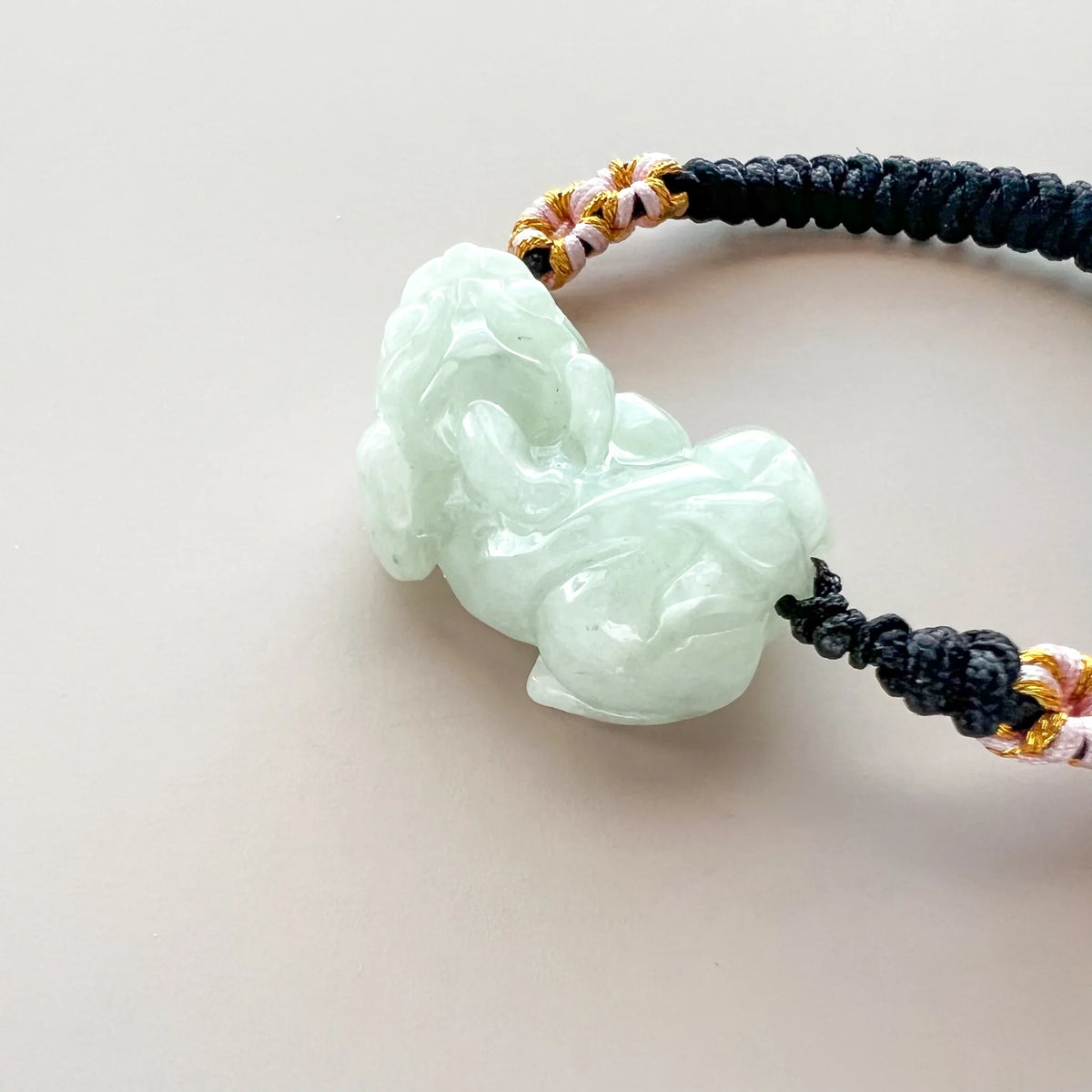 Side close-up of translucent carved jade charm on black cord bracelet