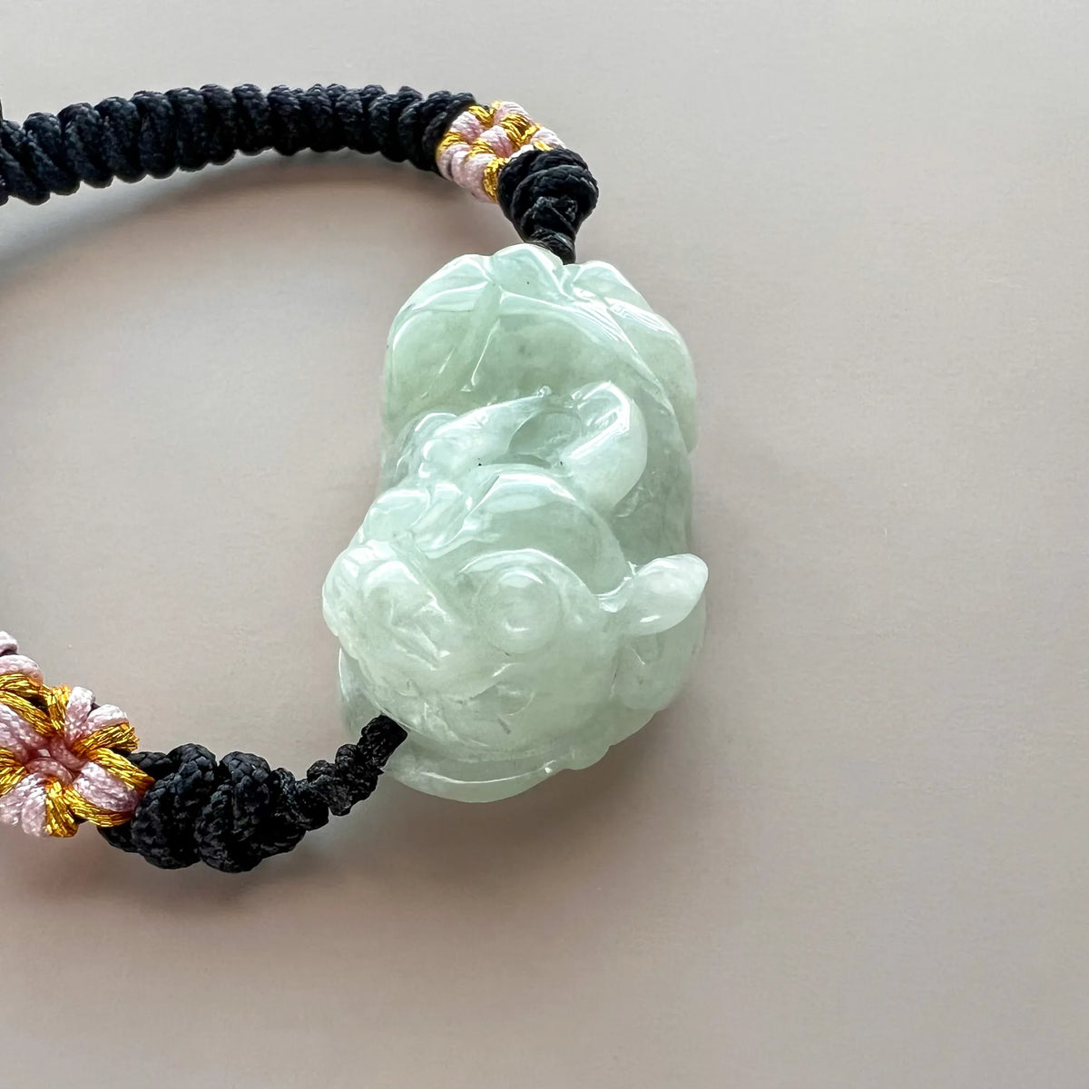 Vertical close-up of polished pale green jade charm and woven cord detail