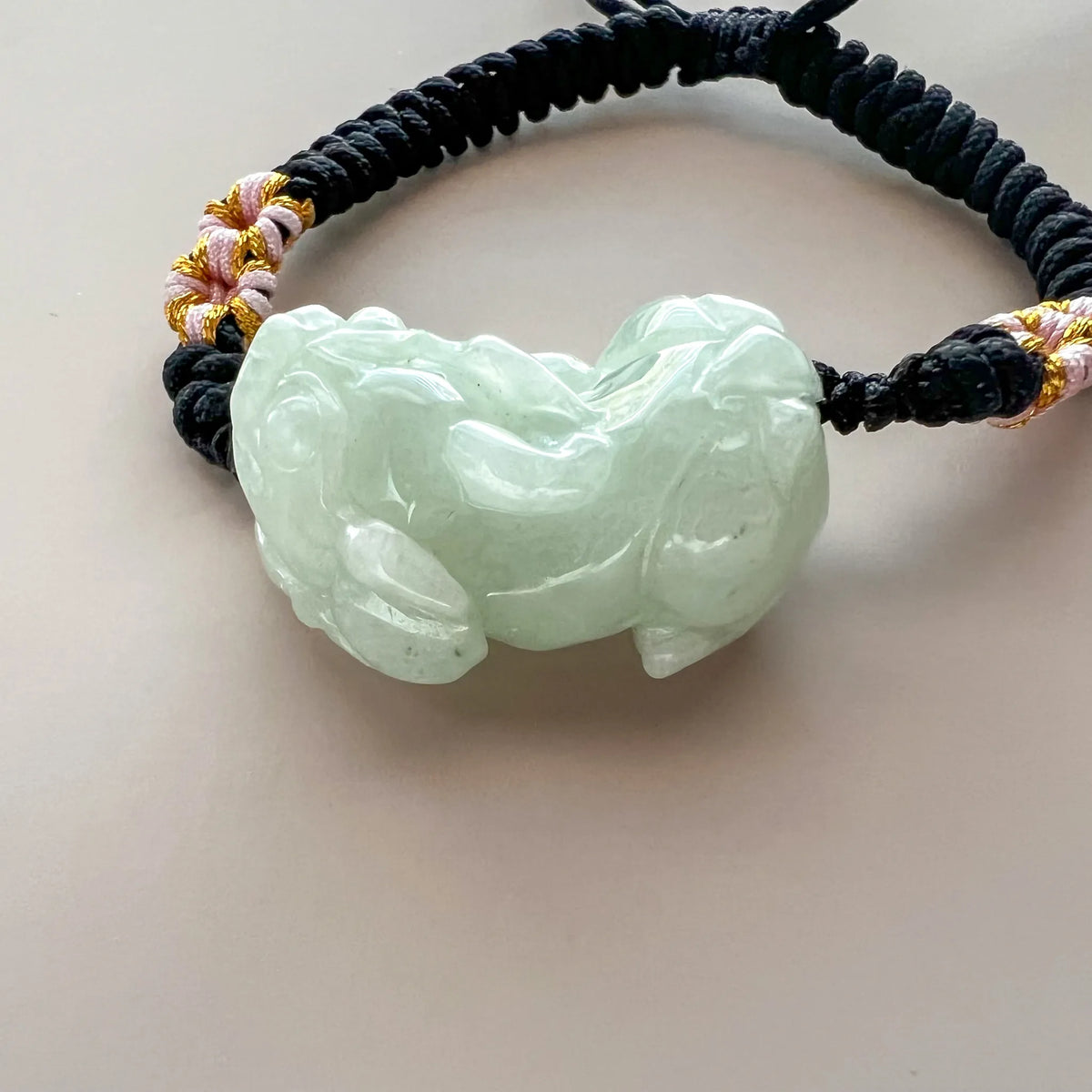 Front close-up of translucent carved jade bracelet with black cord and gold threads