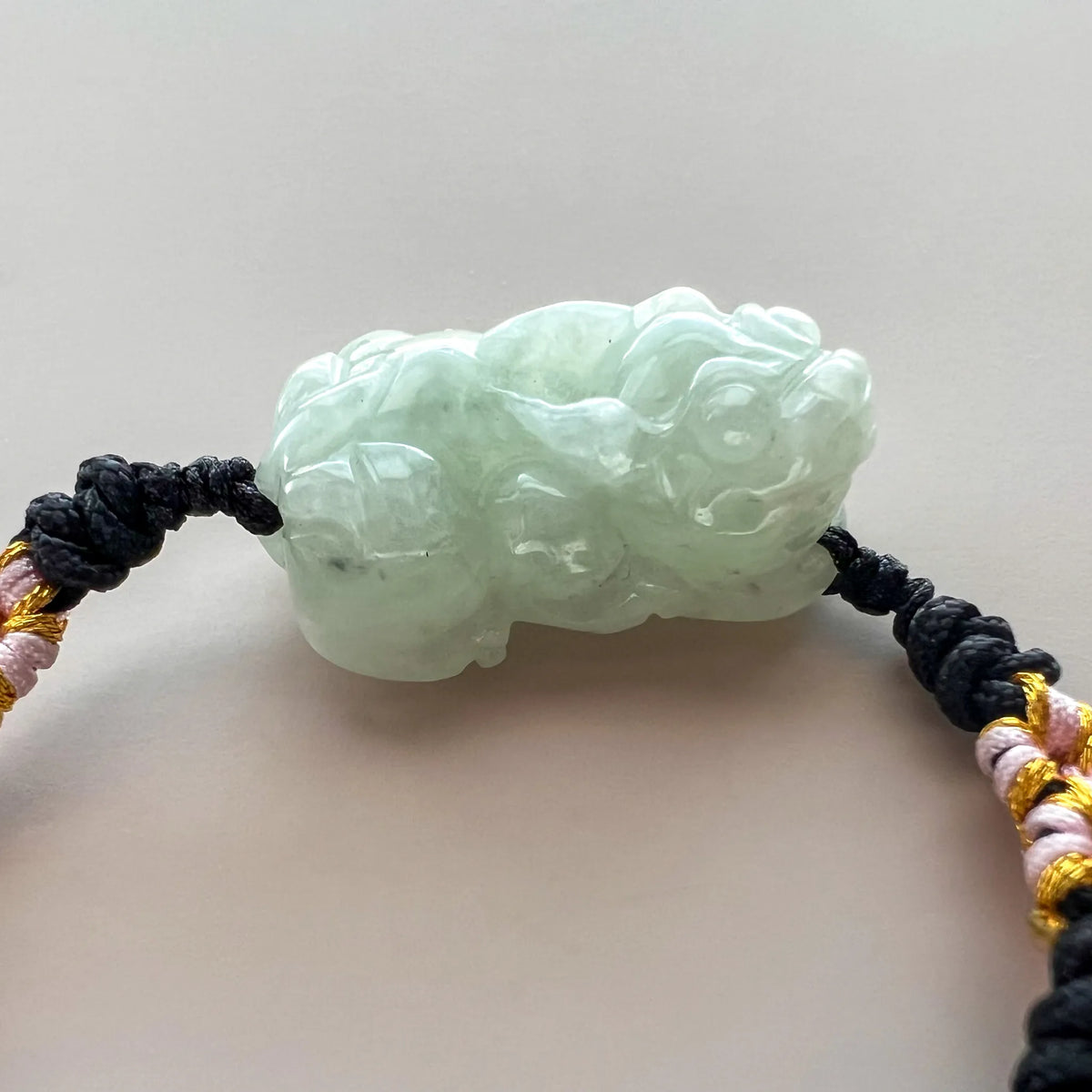 Side profile of carved pale green jade charm on black woven cord
