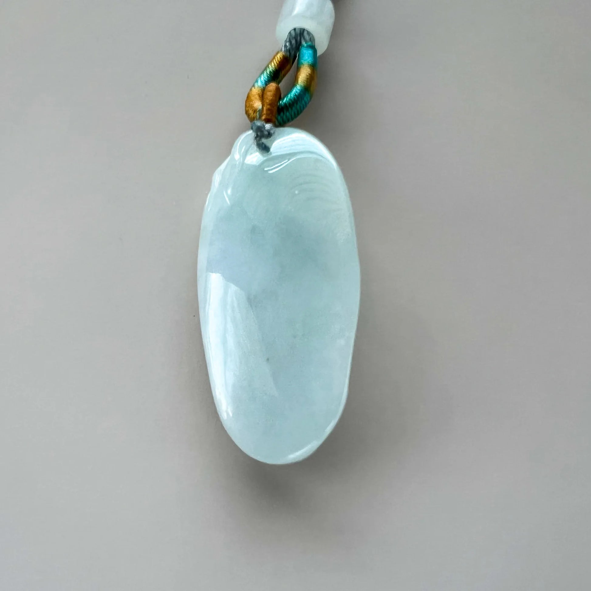 Smooth pale blue-green natural jade pendant reverse with polished finish and multicolor cord loop