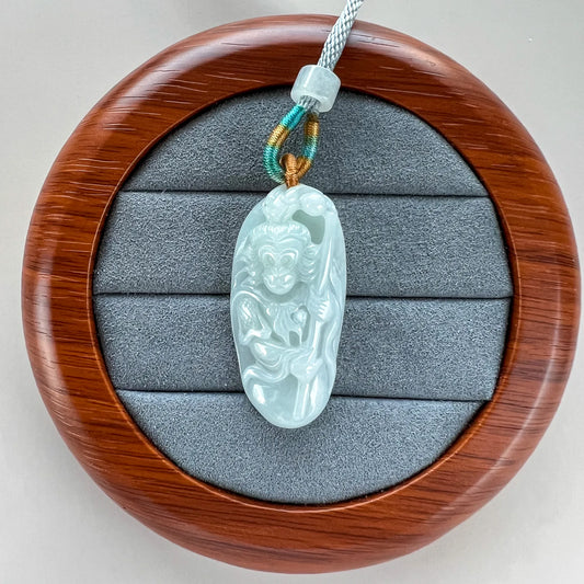 Jade pendant displayed on a round wooden presentation stand, front view with carved figure and polished finish