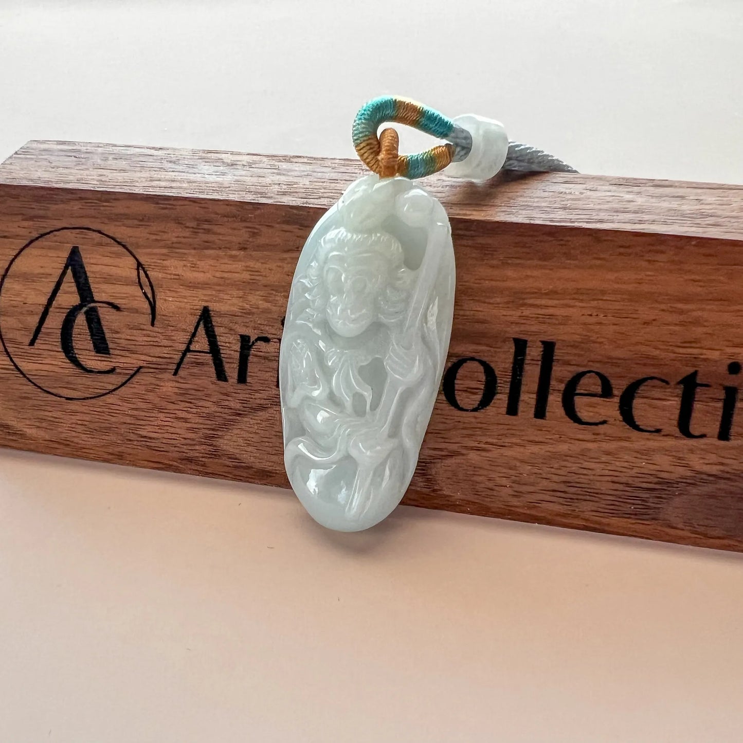 Carved jade pendant photographed on a wooden branded holder, angled front view with glossy finish