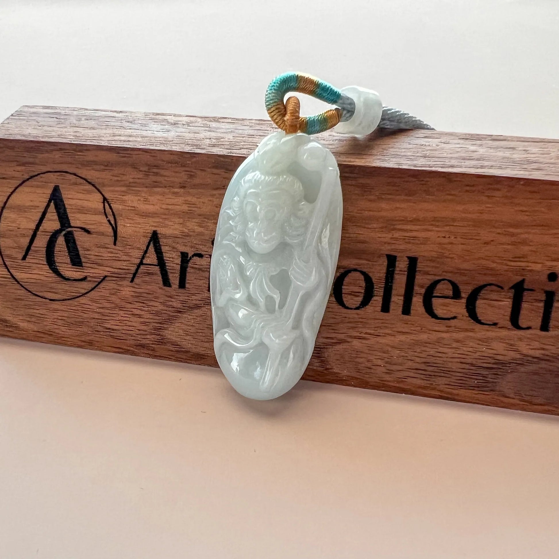 Carved jade pendant photographed on a wooden branded holder, angled front view with glossy finish