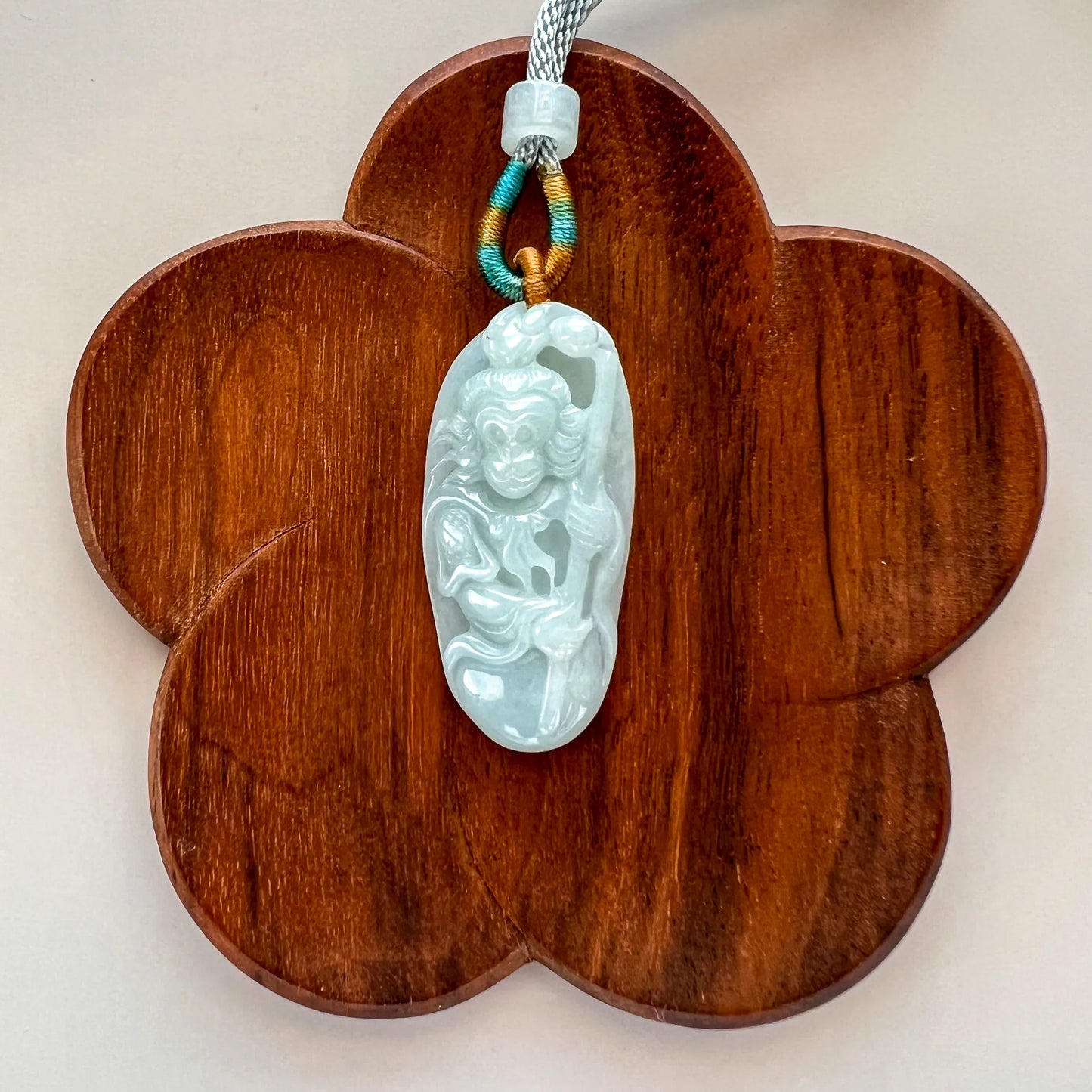 Front view of carved jade pendant on flower-shaped wooden display, polished stone and decorative cord