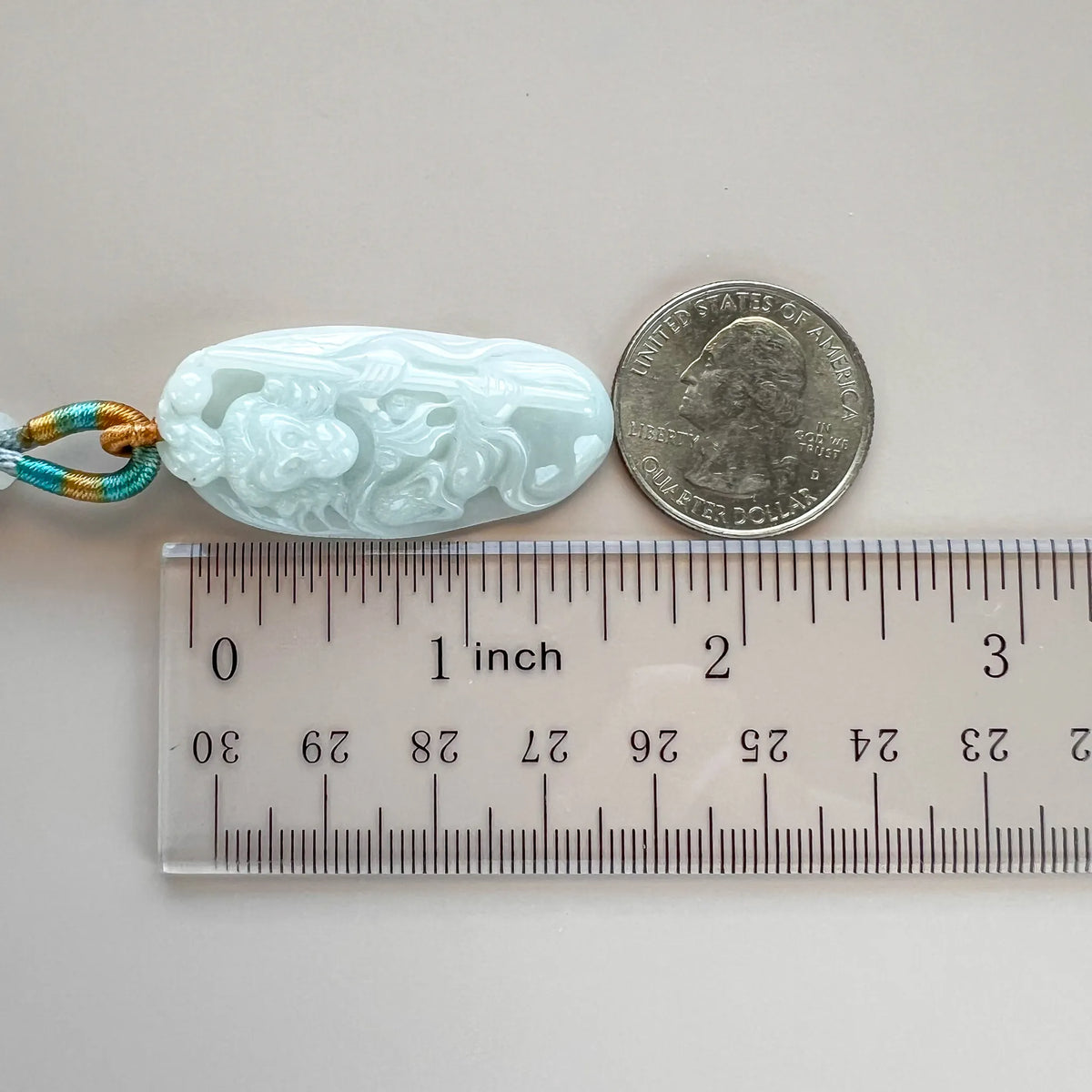 Jade pendant shown with ruler and coin for scale, carved front face and polished light blue stone