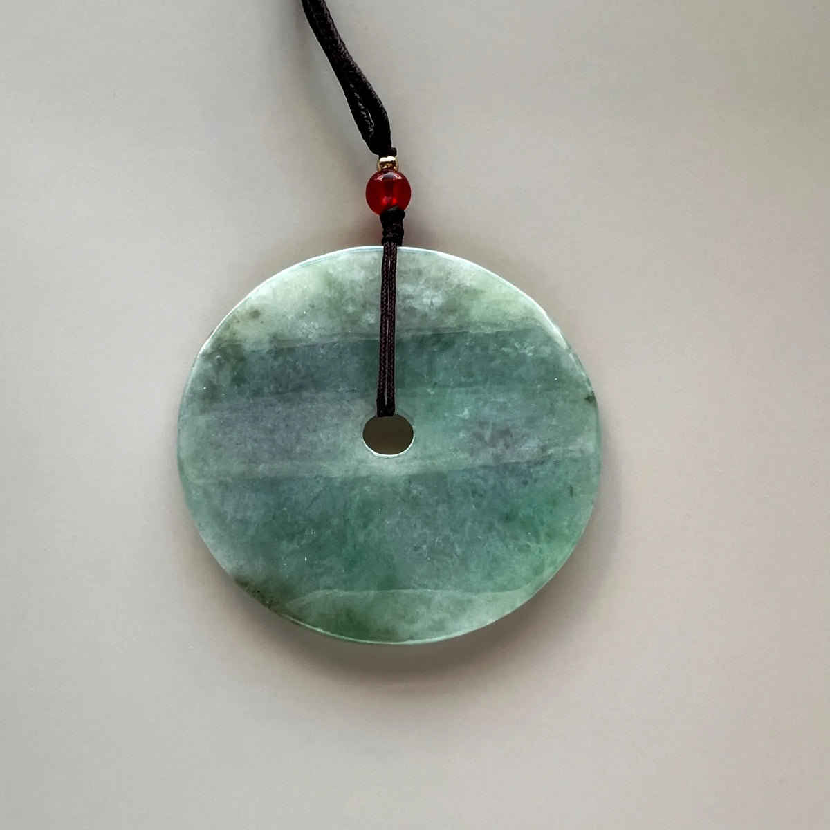Smooth polished back of a pale green natural jade round pendant with central cord opening