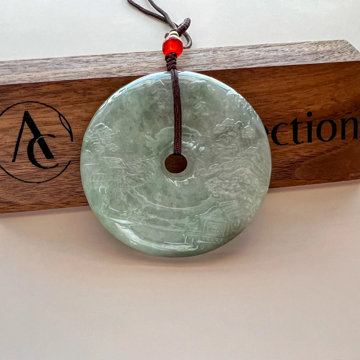 Front view of carved green jade pendant hanging on branded wooden display plaque