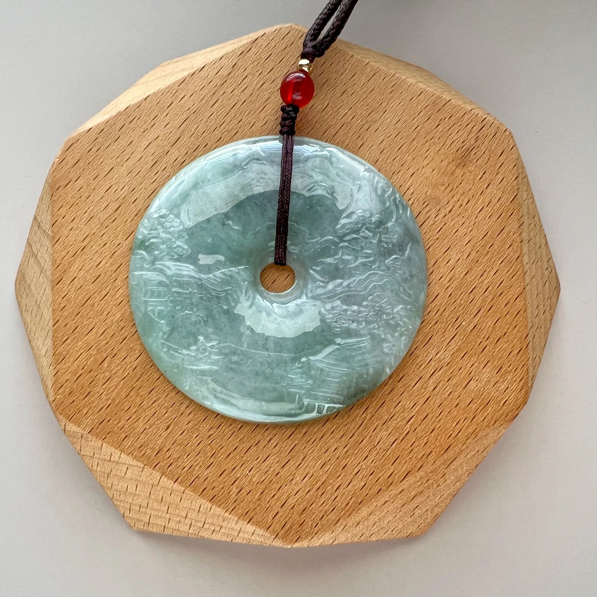 Green jade disc pendant on faceted light wood stand, polished carved surface visible