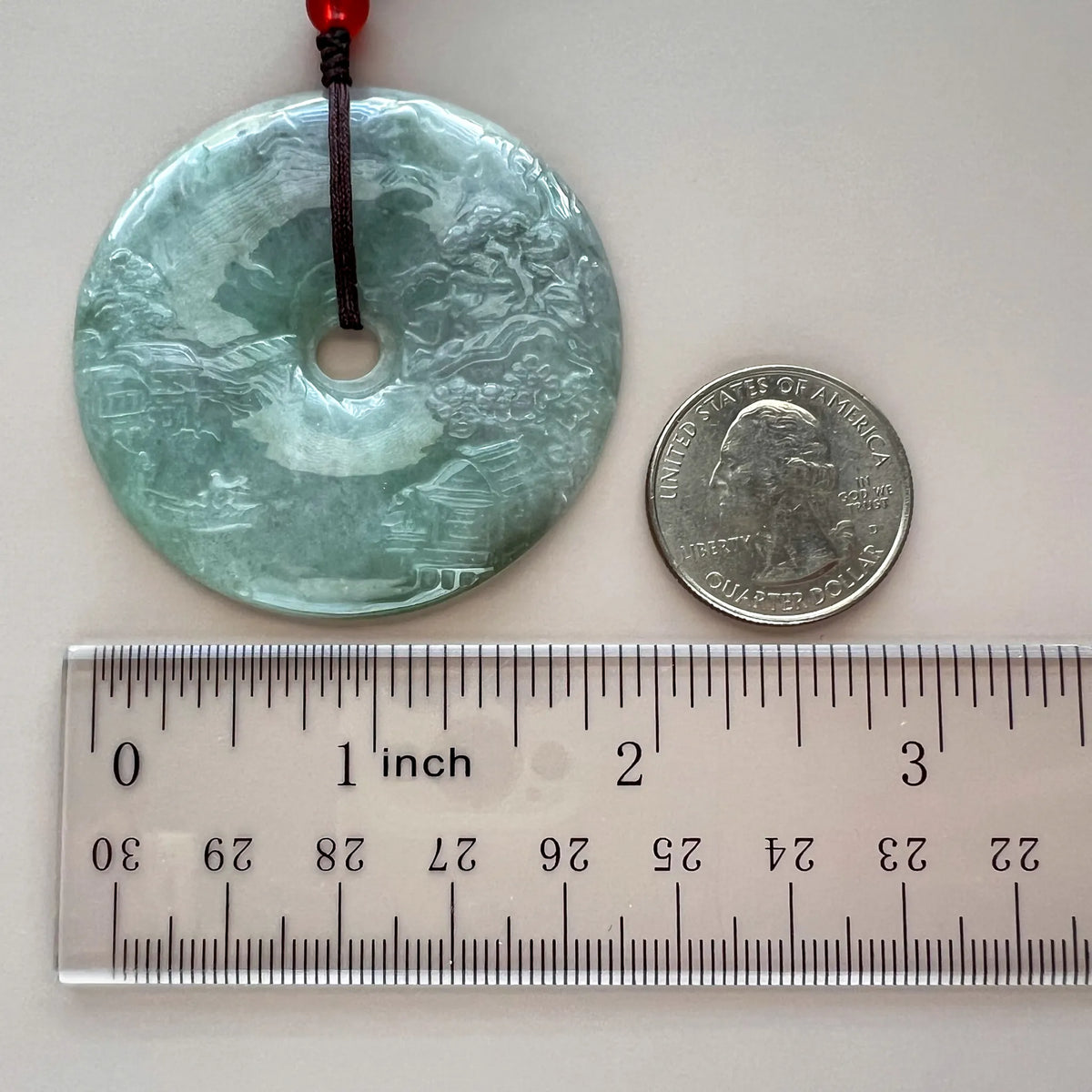 Jade pendant with ruler and quarter for scale, showing round disc size and textured carving