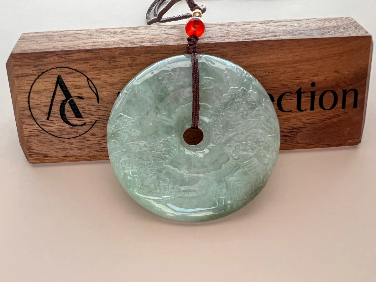 Front pendant on branded wood plaque, glossy carved jade disc with hanging cord and red accent bead
