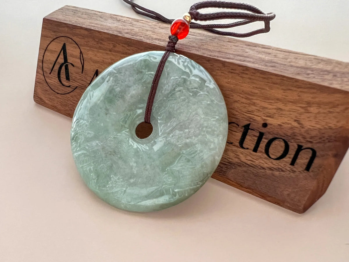 Angled back view of jade disc pendant on branded wood plaque, polished green stone and cord visible